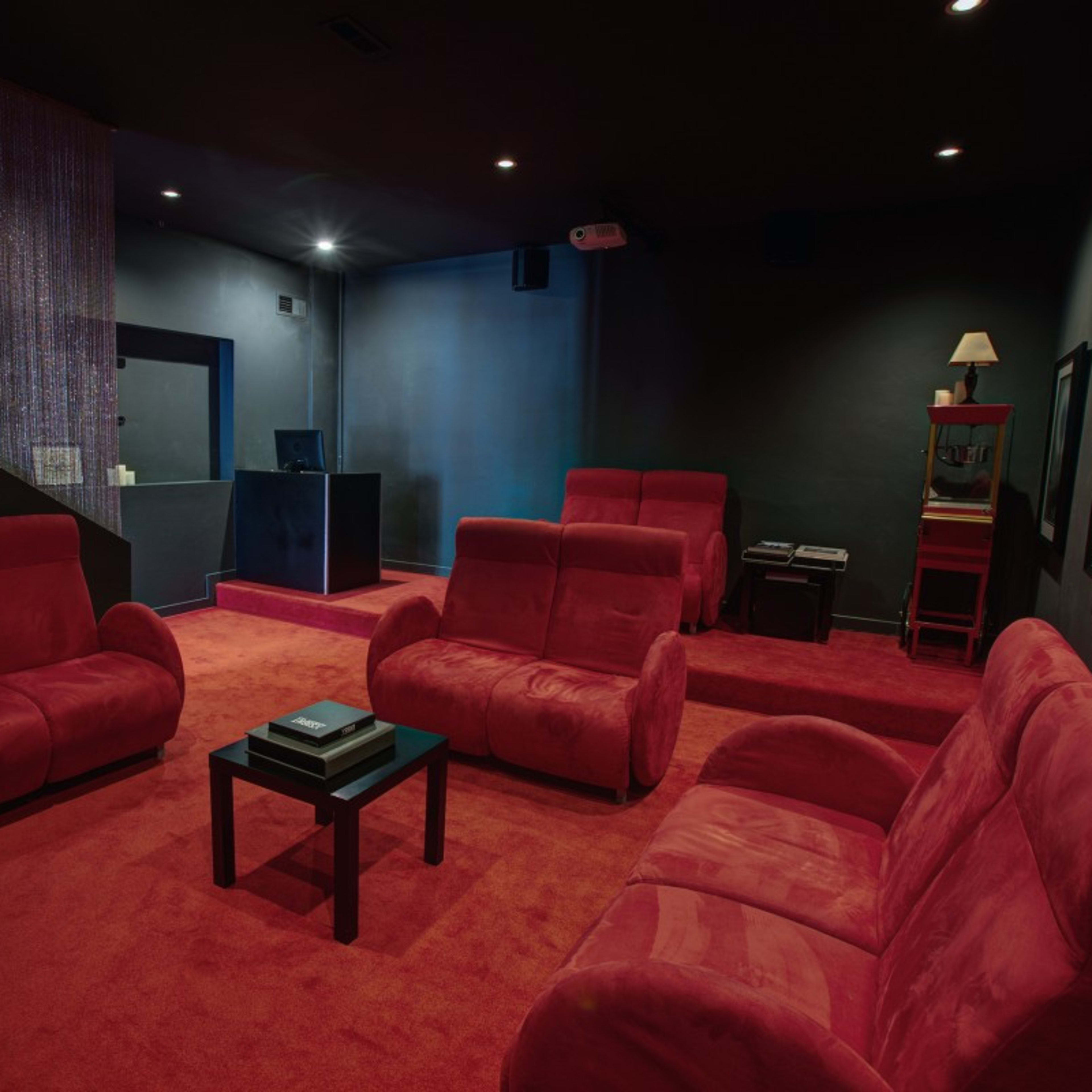 A dimly lit lounge area with four red couches arranged around a small black table on a red carpet.