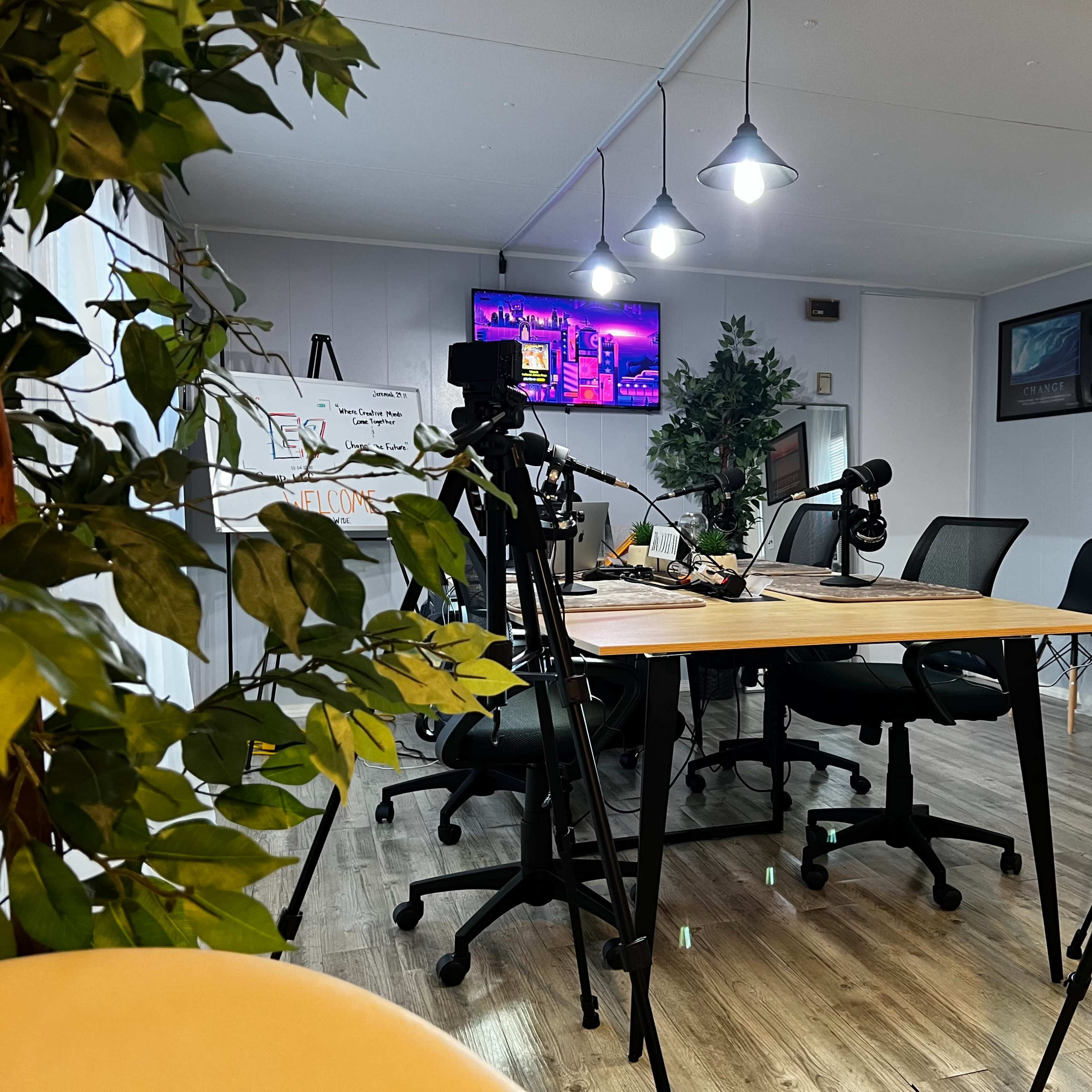 A modern meeting room equipped with cameras on tripods, a large table, and a television displaying a colorful graphic in the background.