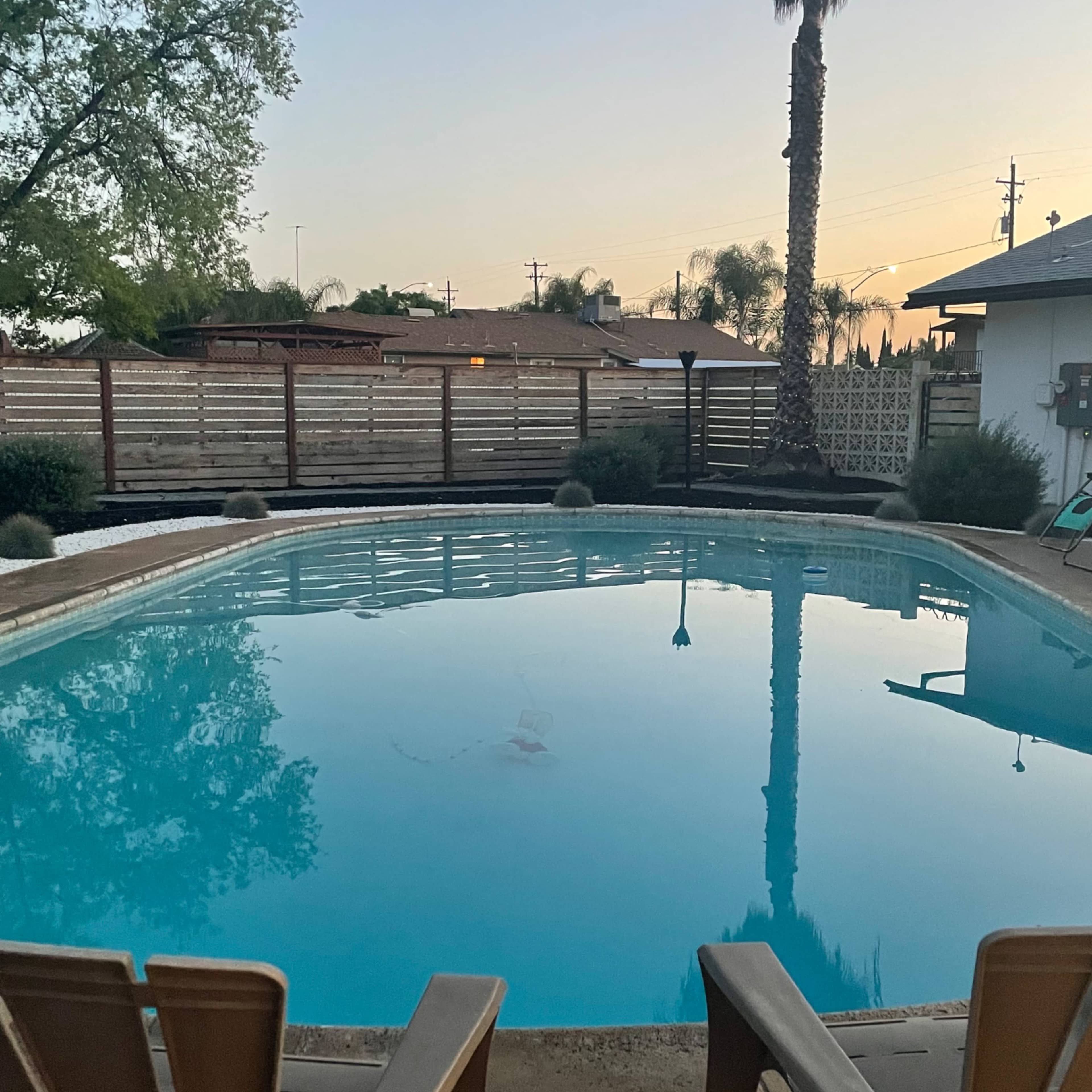 A tranquil swimming pool surrounded by a patio area and palm trees at dusk.