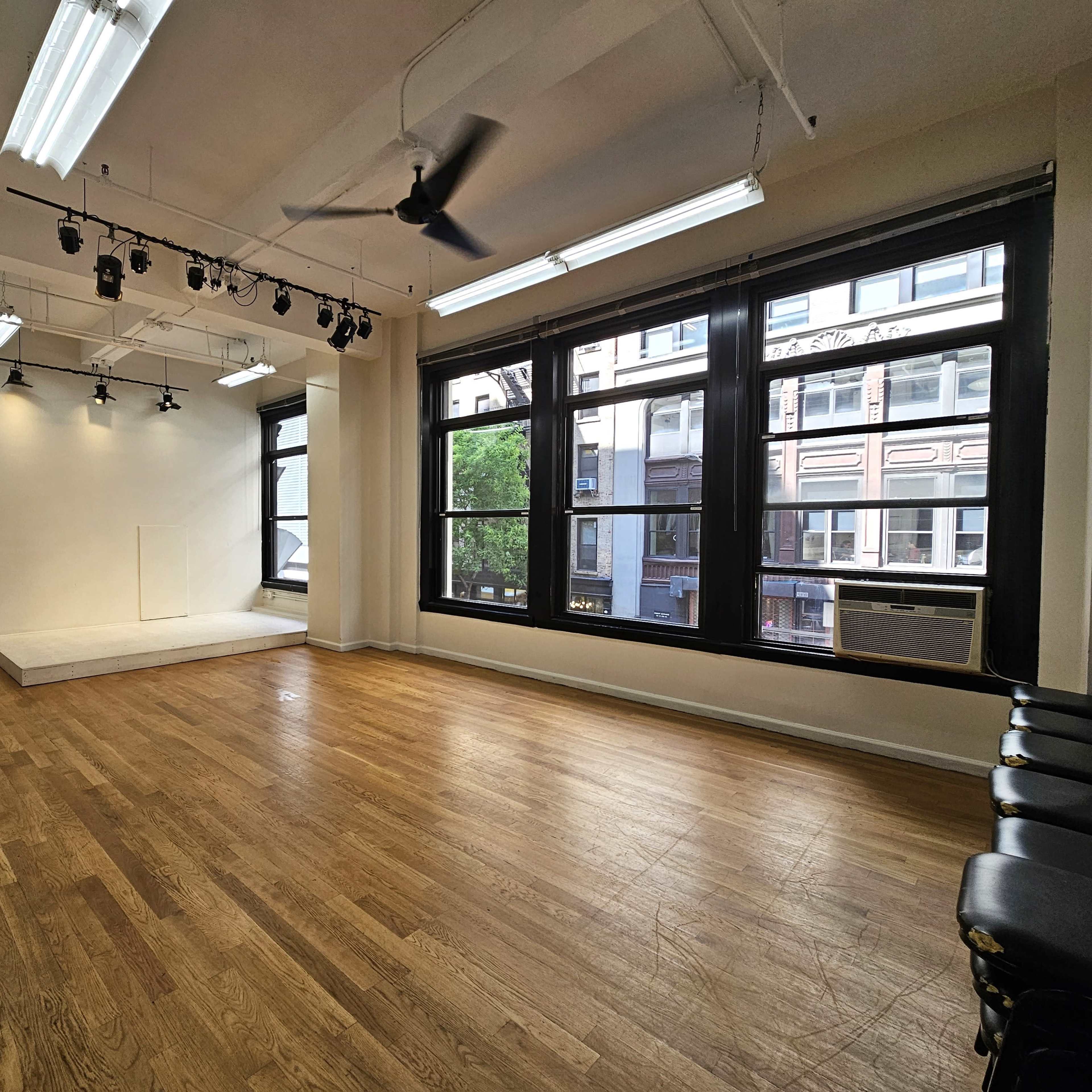 An empty room with wooden floors, large windows, and a raised platform in one corner.