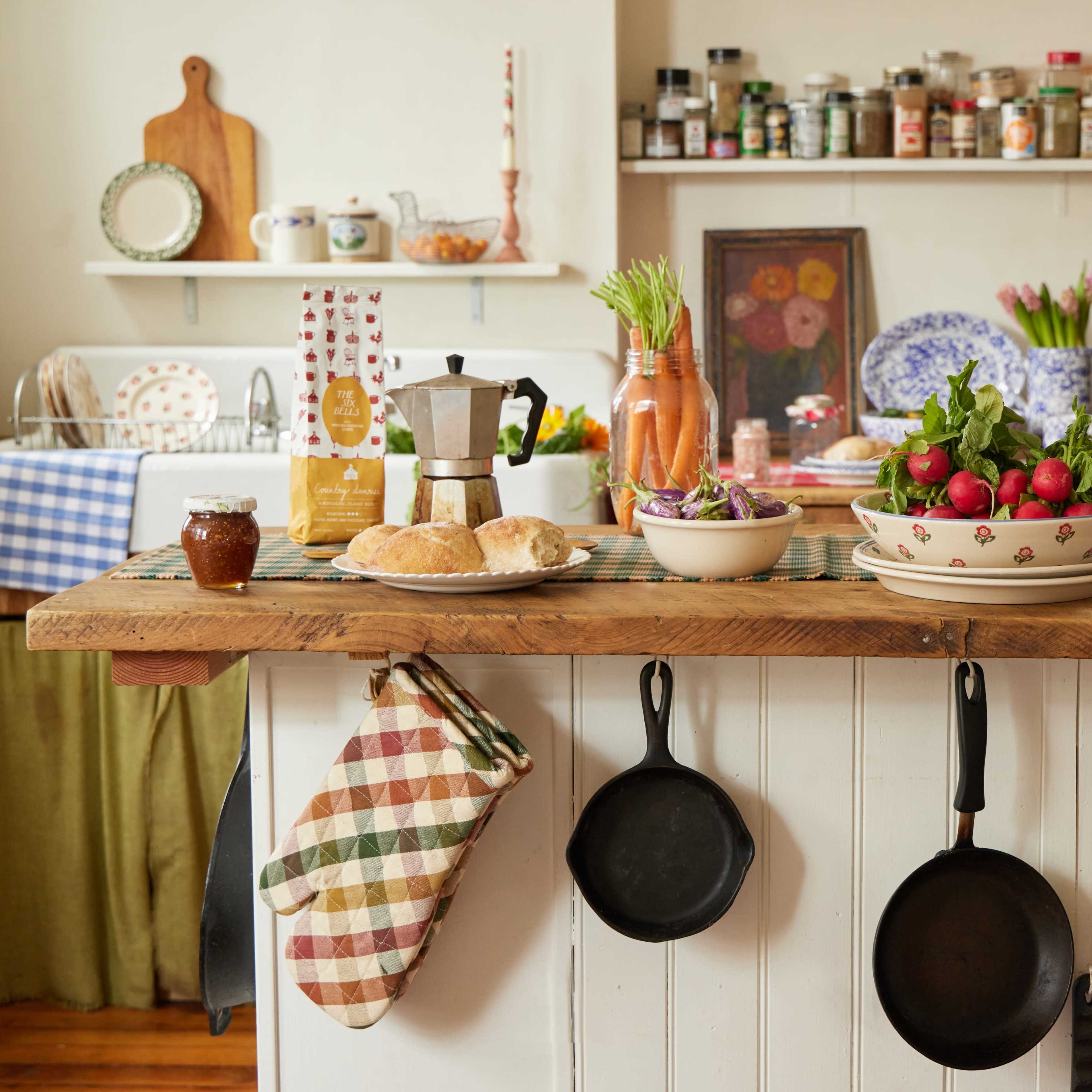 A rustic kitchen countertop is adorned with fresh vegetables, baked bread, and cooking utensils, while spices and jars line the shelves in the background.