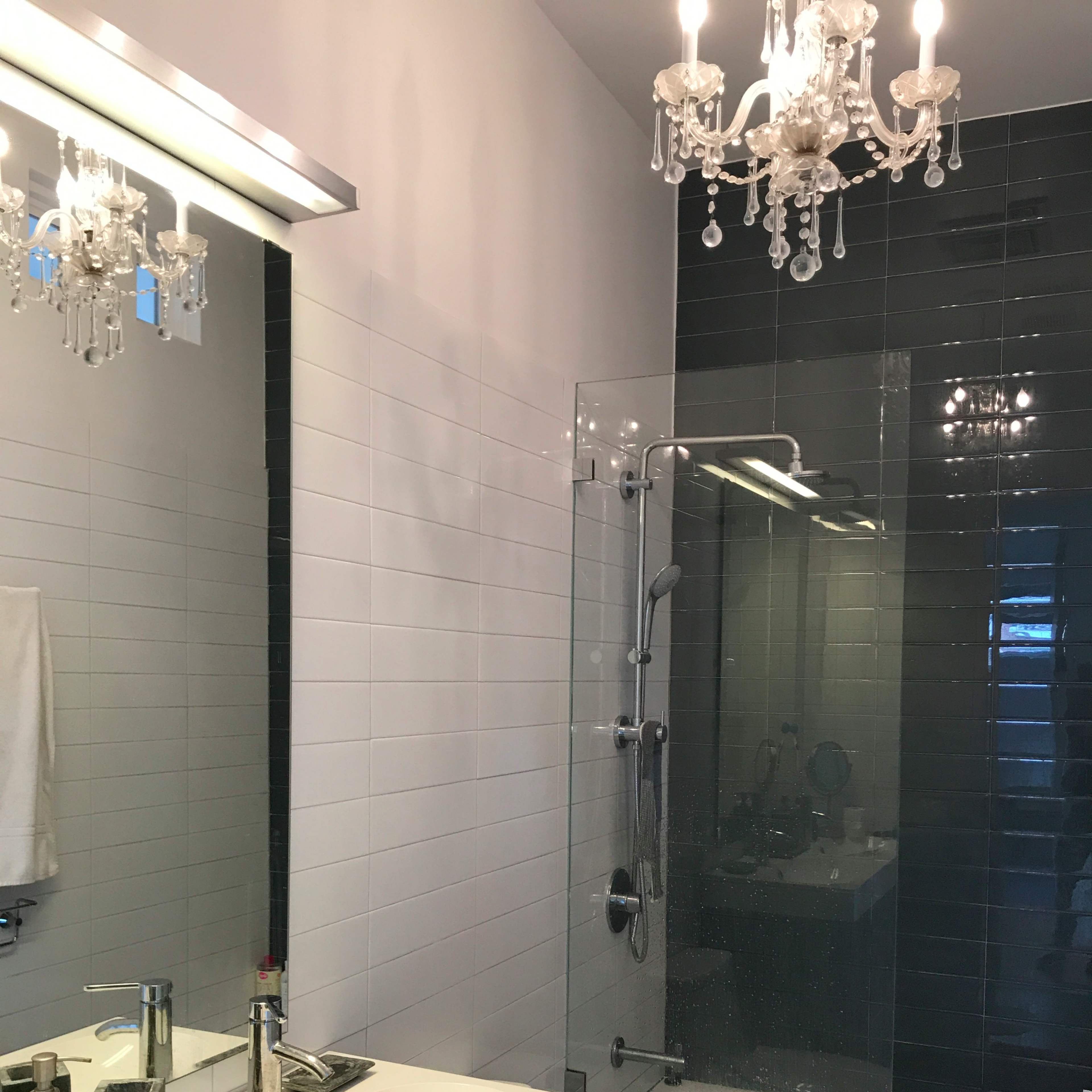A modern bathroom featuring a glass shower, a white countertop with a sink, and a chandelier above.