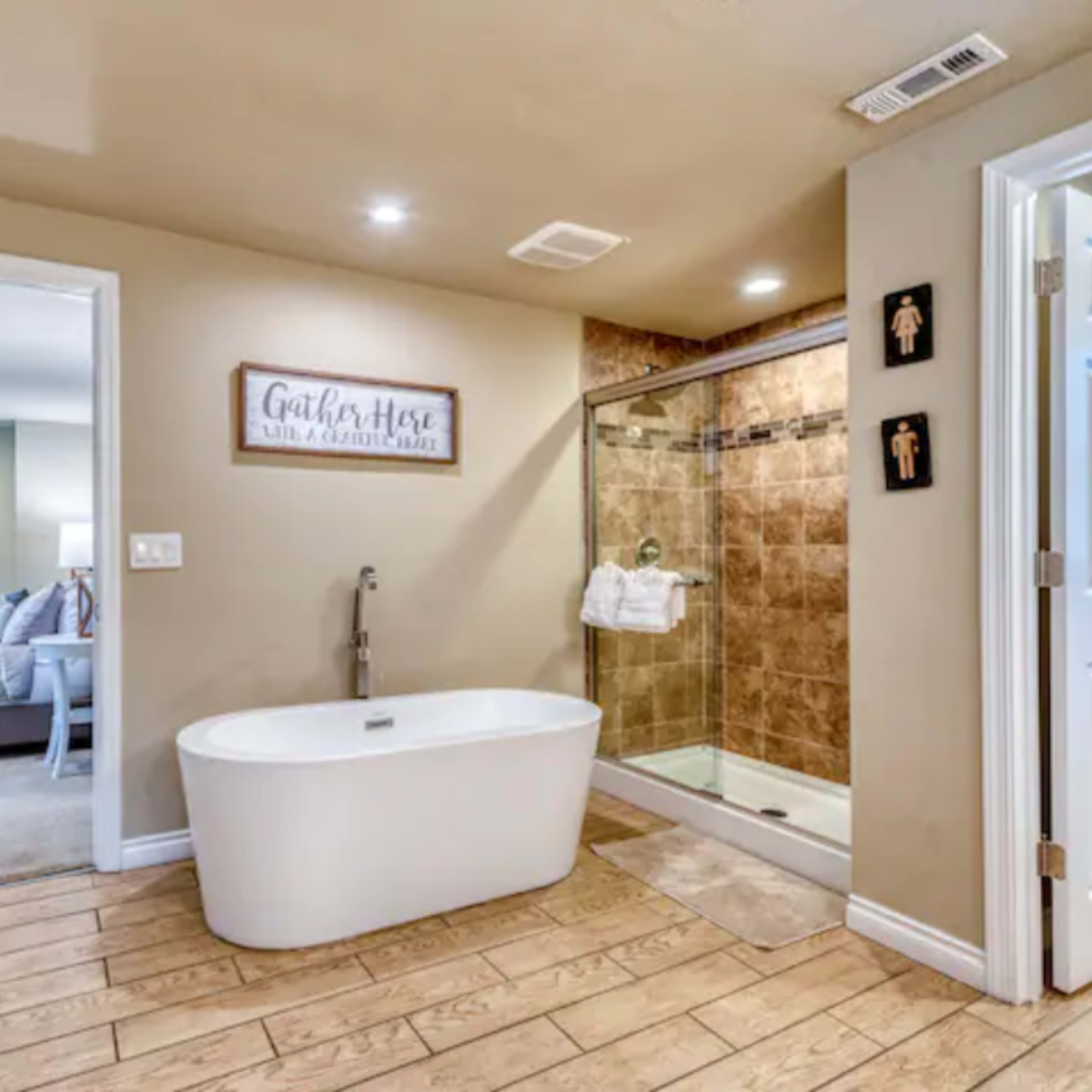 A modern bathroom features a freestanding bathtub beside a glass shower enclosure, with a door leading to another room.