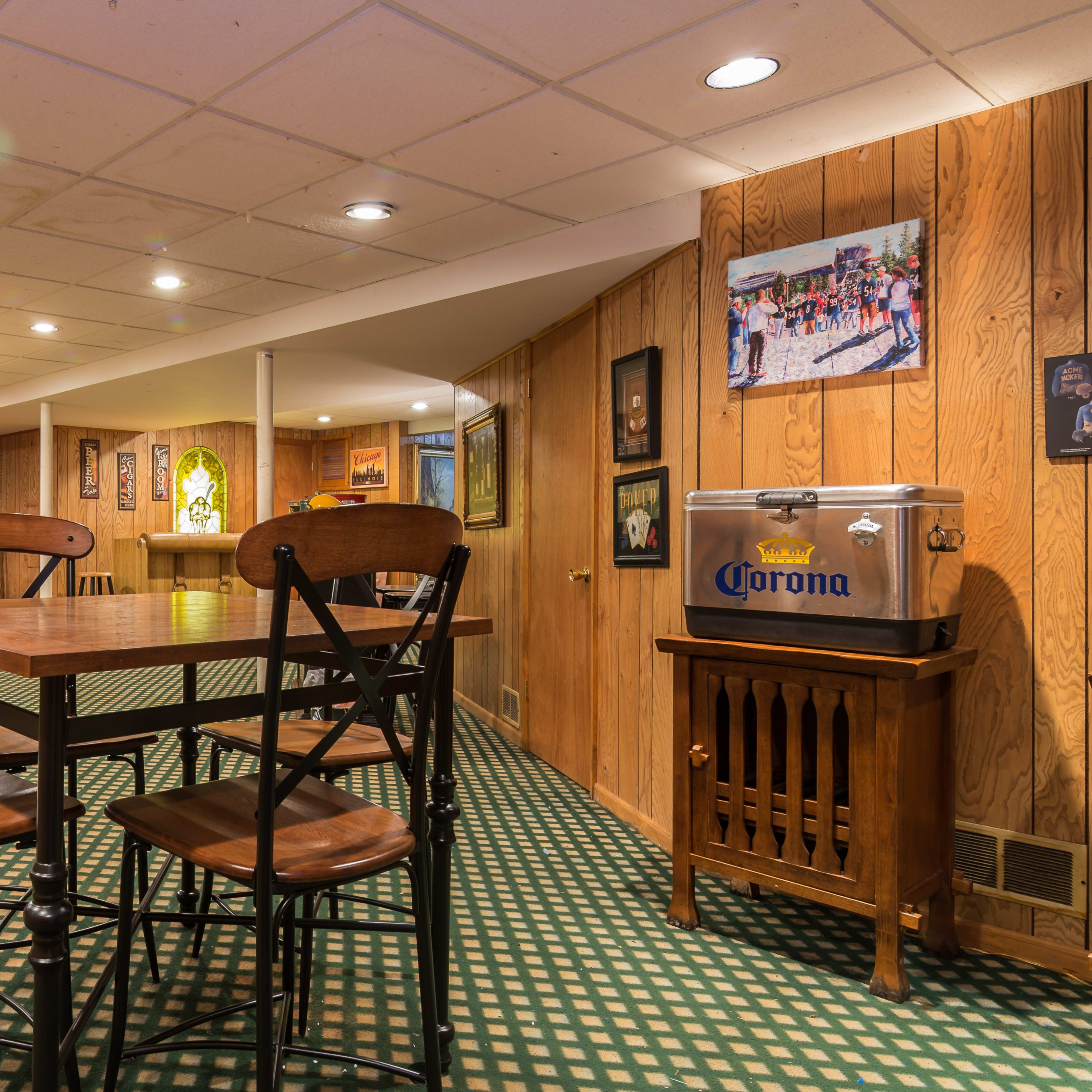 A dimly lit basement recreation area with wooden paneling, several tables and chairs, and framed photographs on the walls.