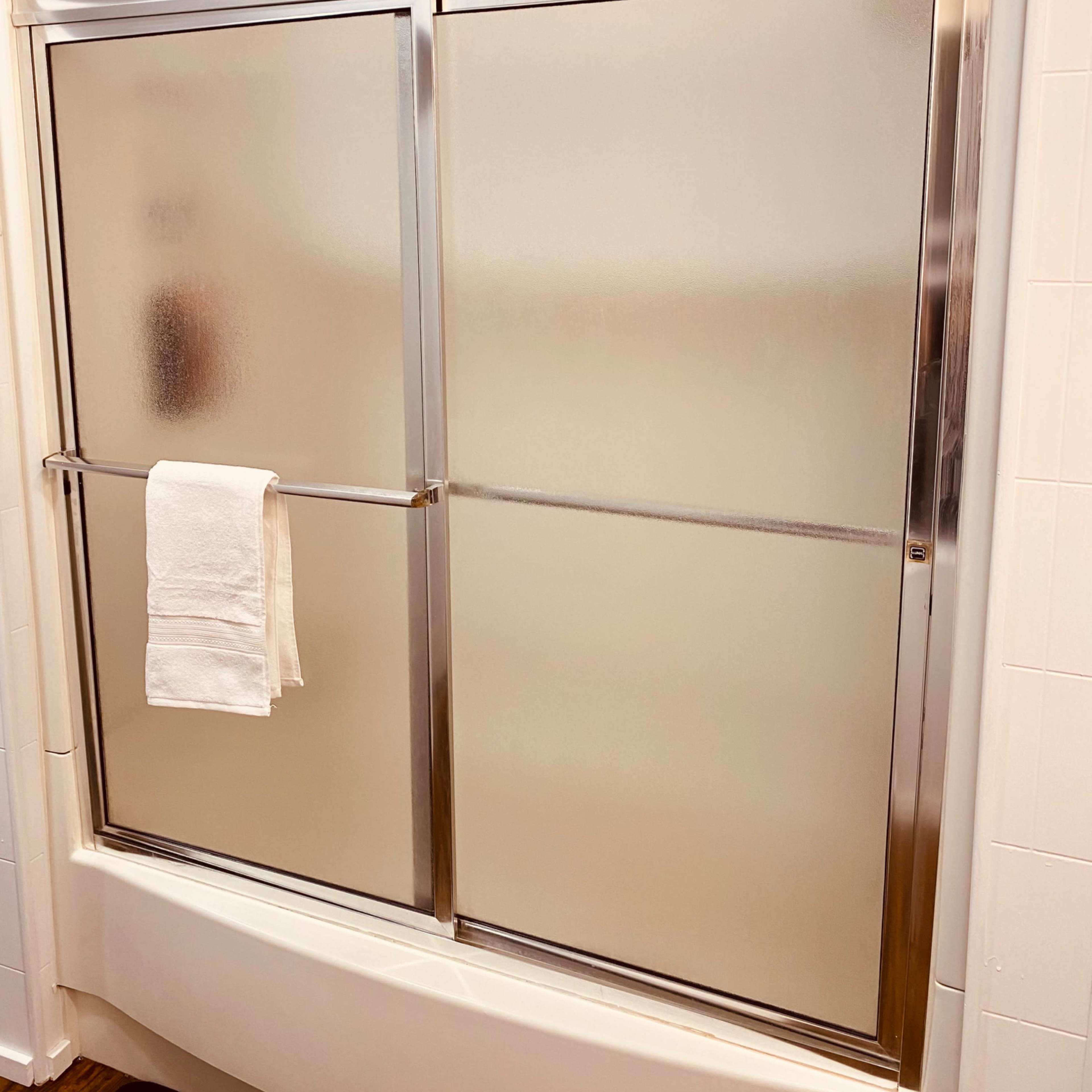 A frosted glass shower door with a metallic frame and a white towel hanging on the bar.