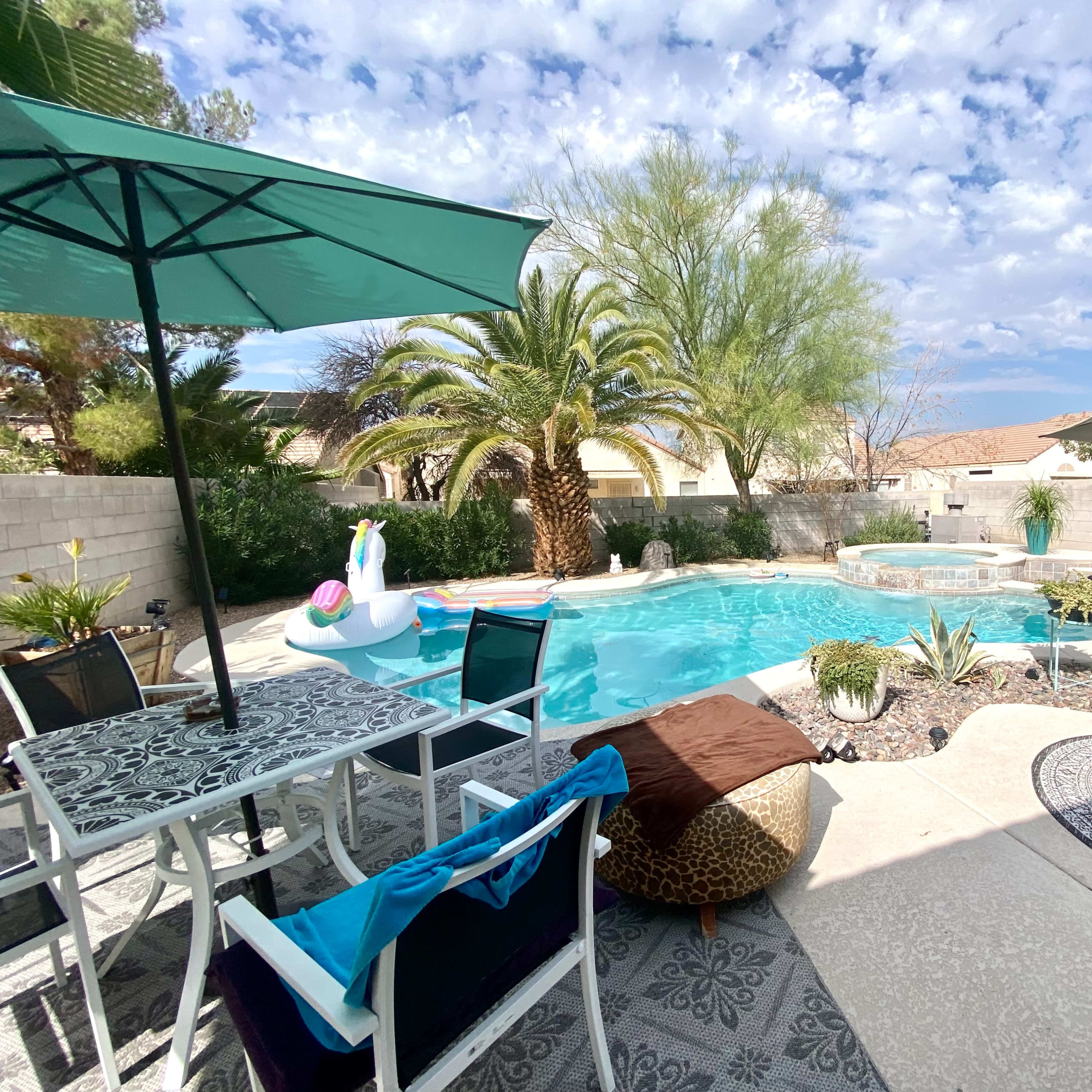 The scene features a backyard pool area with a turquoise swimming pool, lounge chairs, an umbrella, and surrounding greenery.