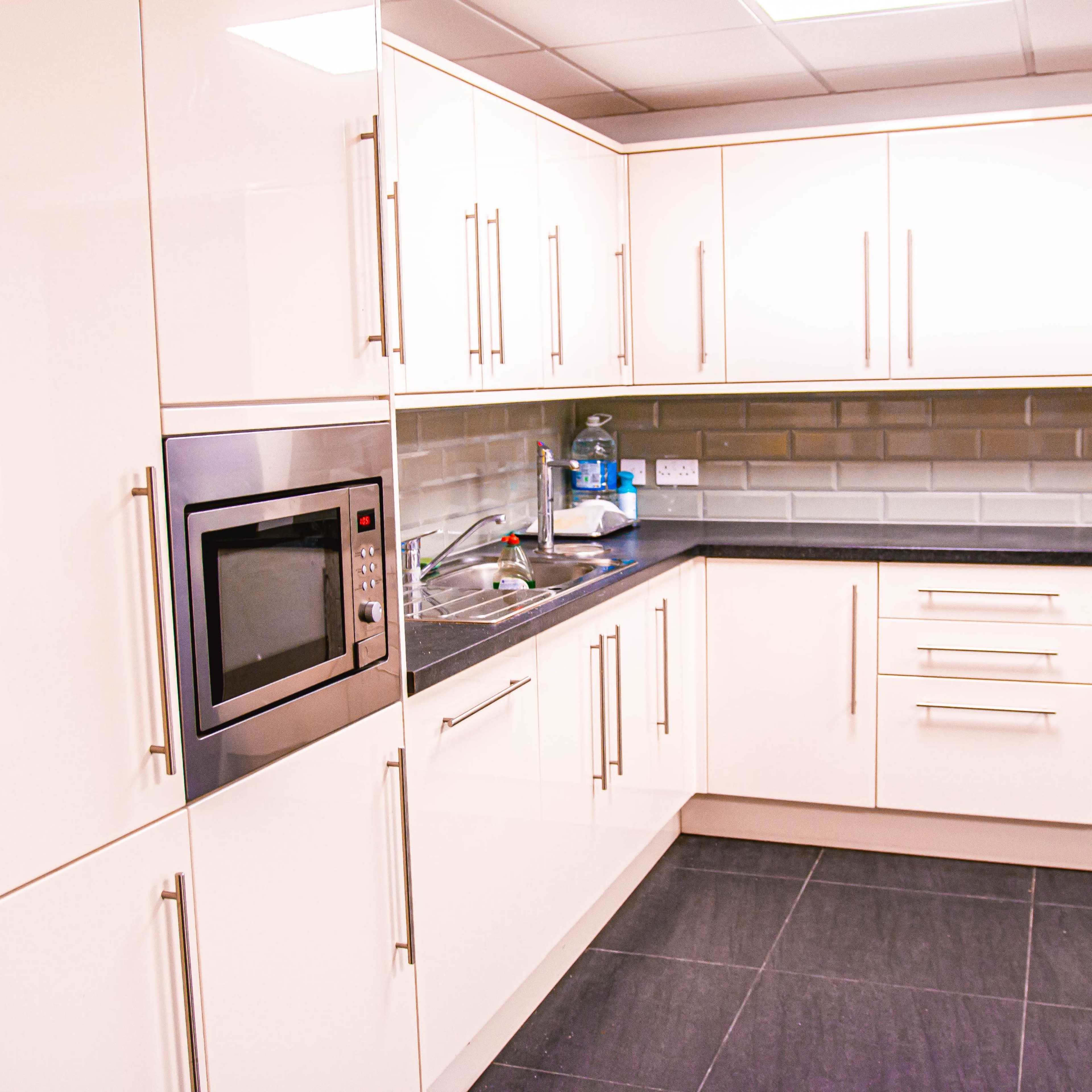 A modern kitchen with sleek white cabinets, a gray tiled backsplash, and stainless steel appliances.