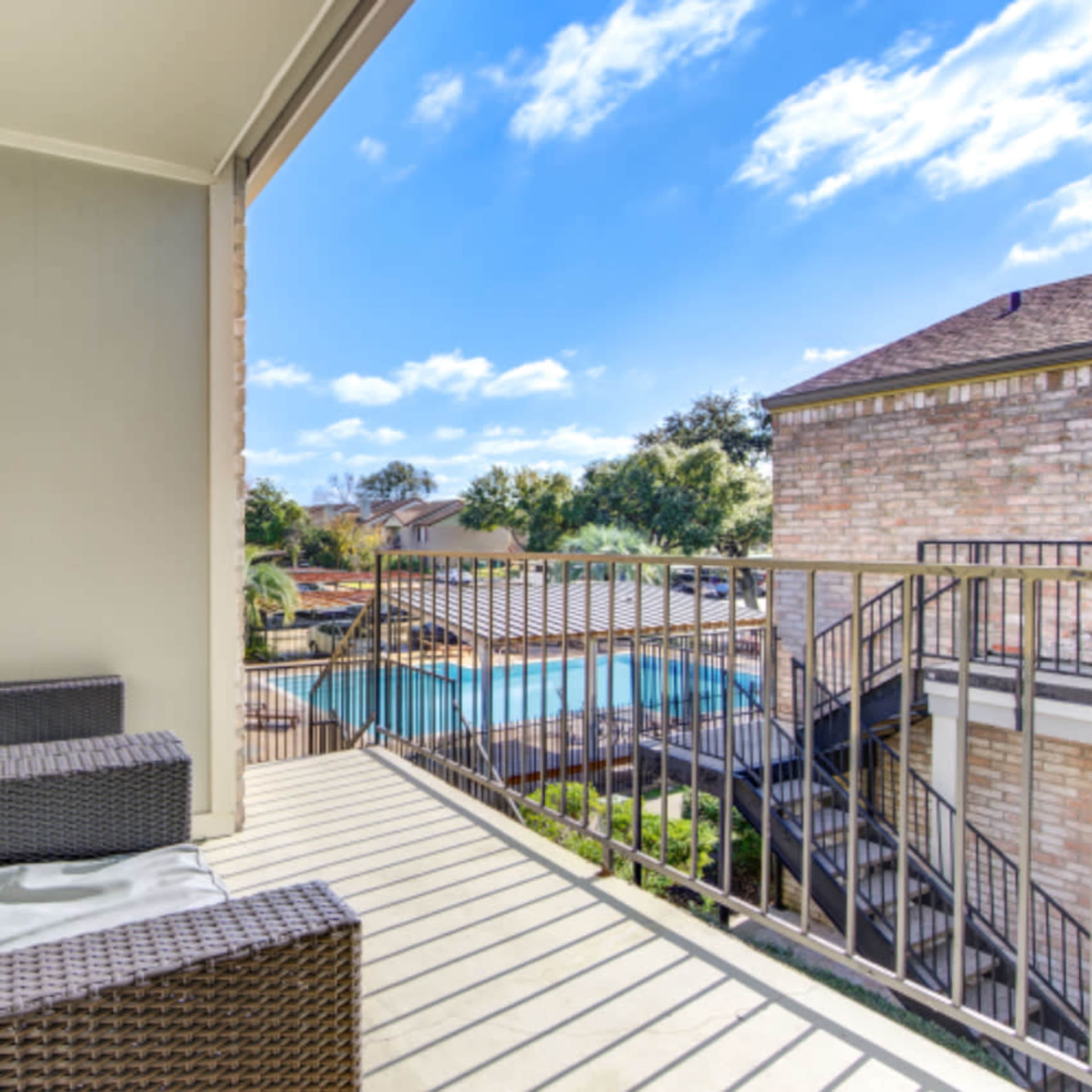 A balcony with two woven chairs overlooks a swimming pool and landscaped area under a clear blue sky.