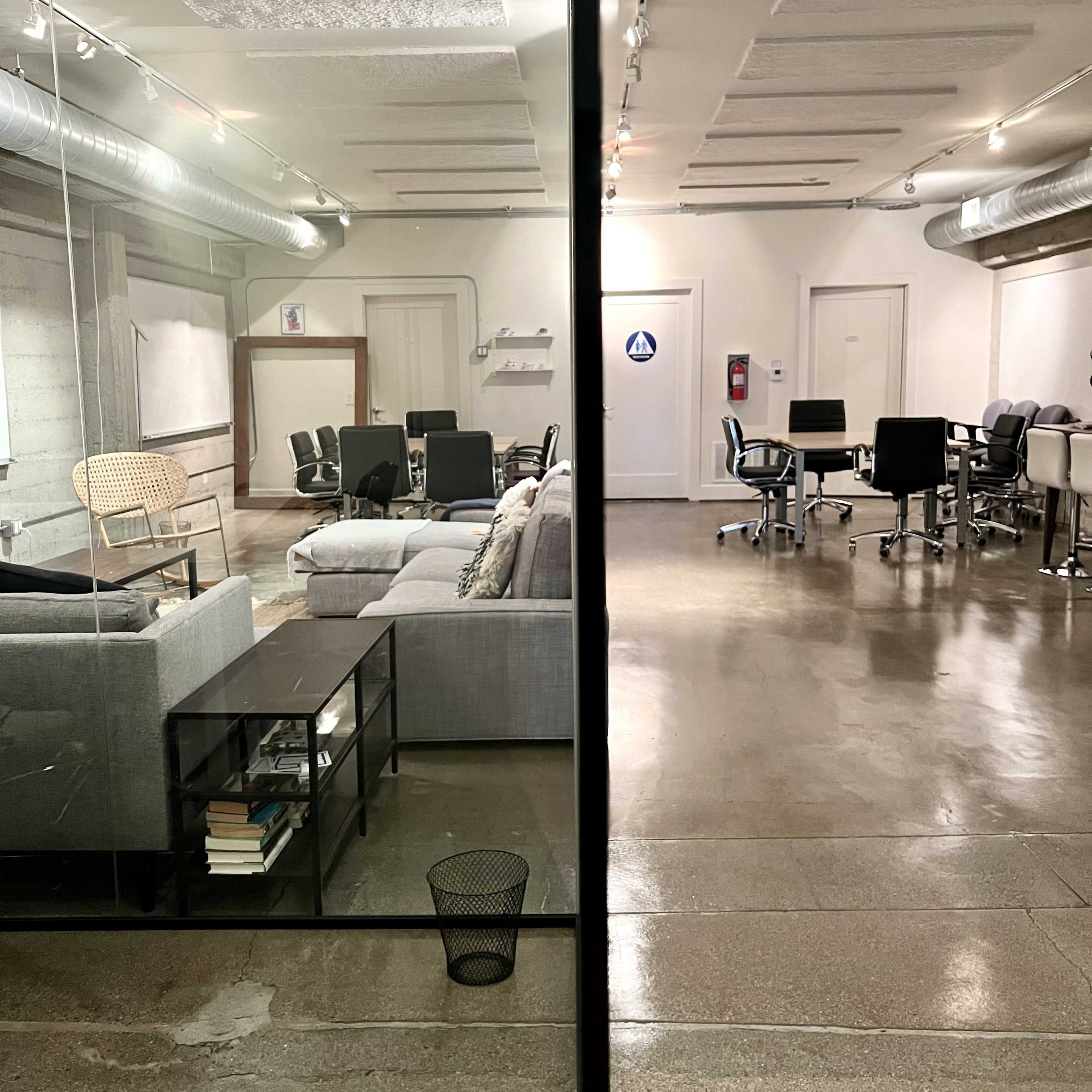 A divided office space, with a casual seating area on one side and a formal work area with desks and chairs on the other.