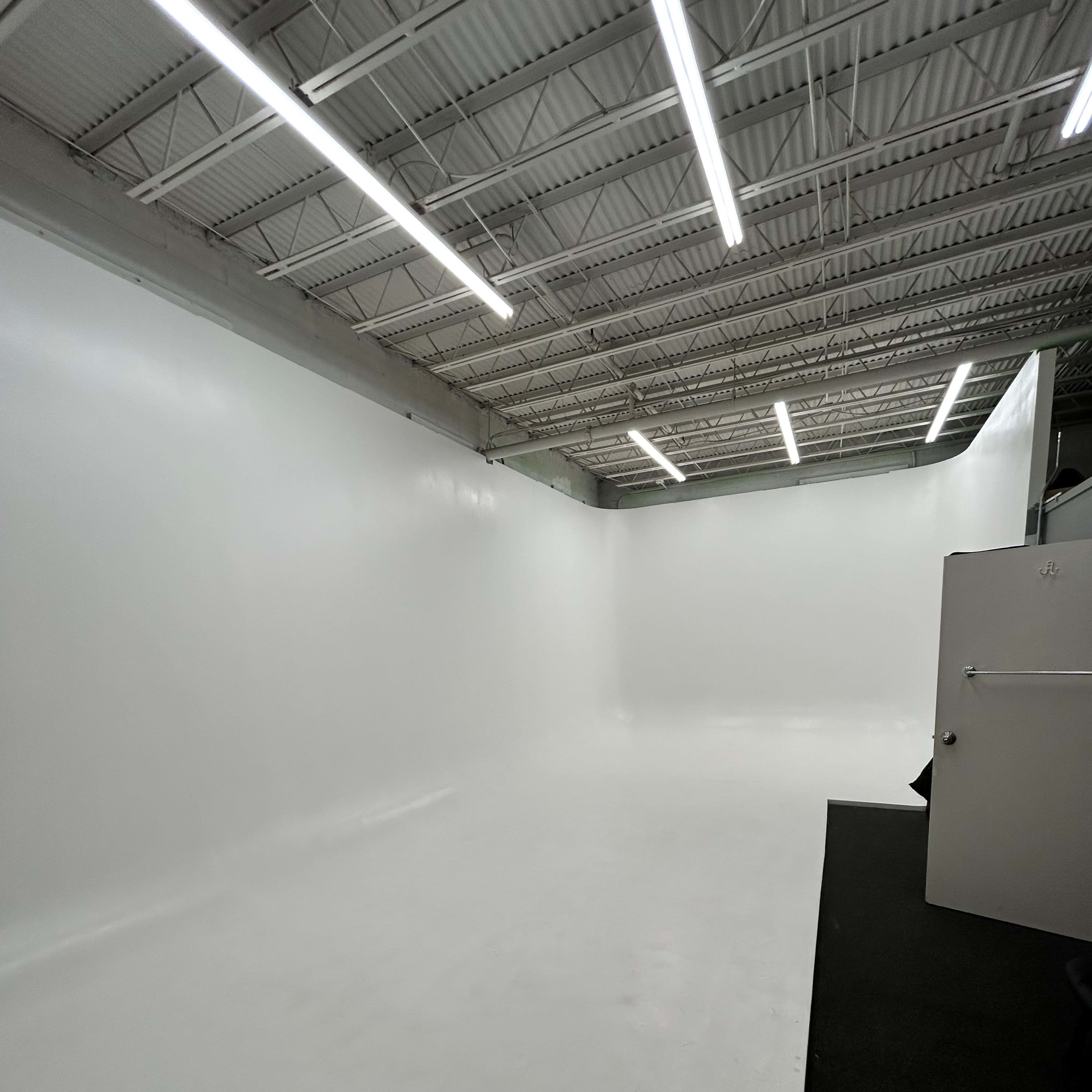 A large, empty studio with white walls and flooring, illuminated by bright overhead lights.
