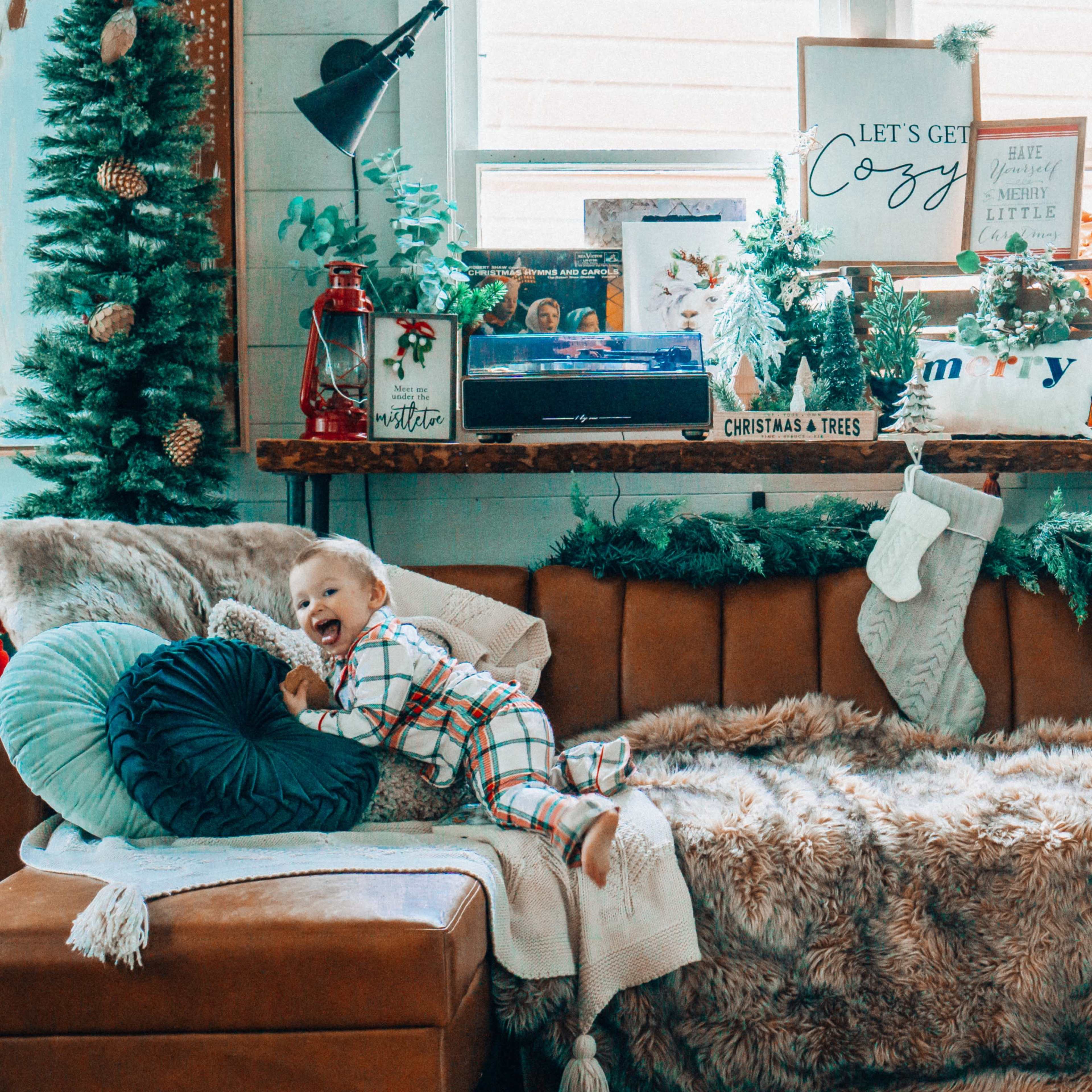 A child in festive pajamas plays on a cozy brown couch adorned with holiday decorations and throws.