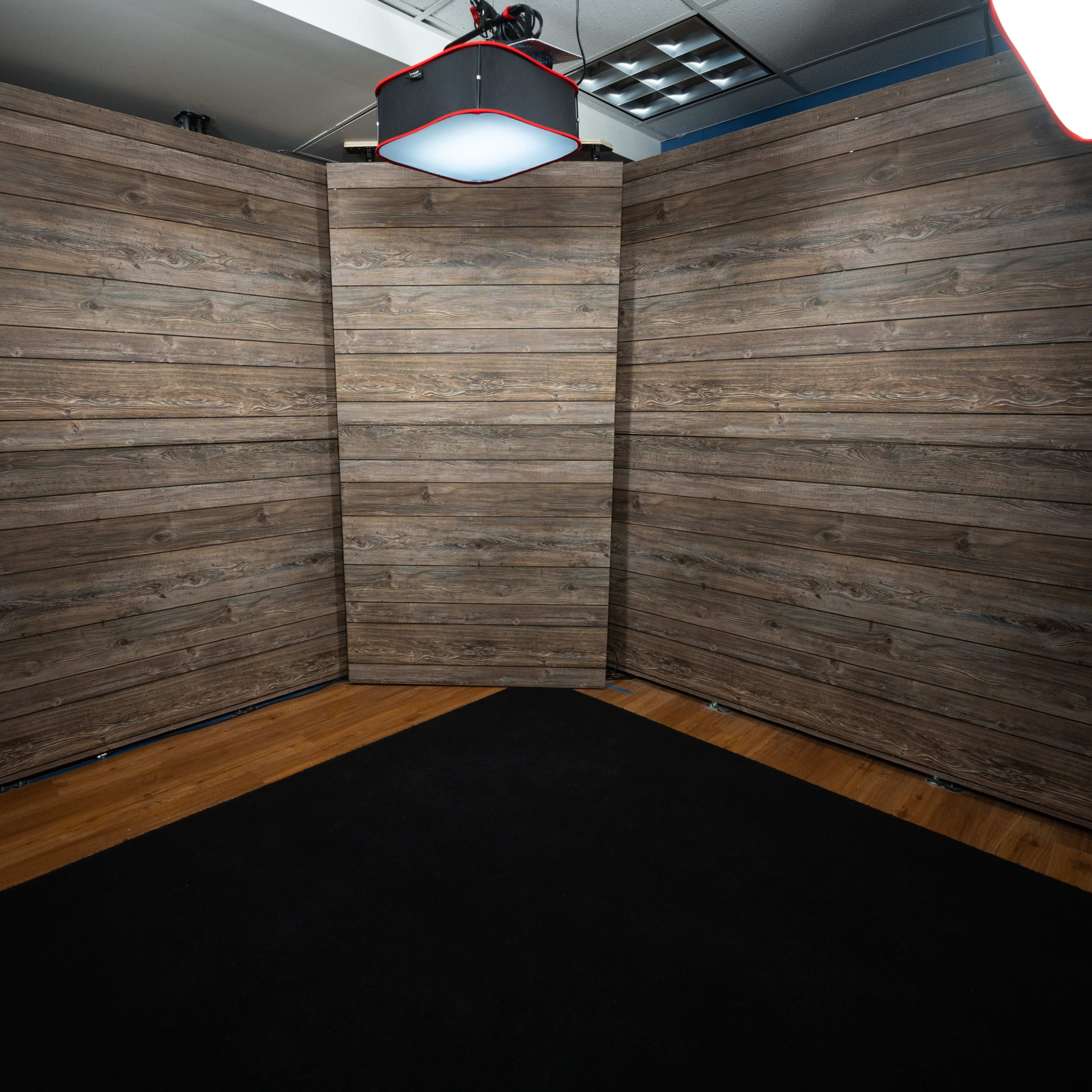 A studio setup with three wood-paneled backdrops positioned at angles, surrounded by a black carpeted floor.
