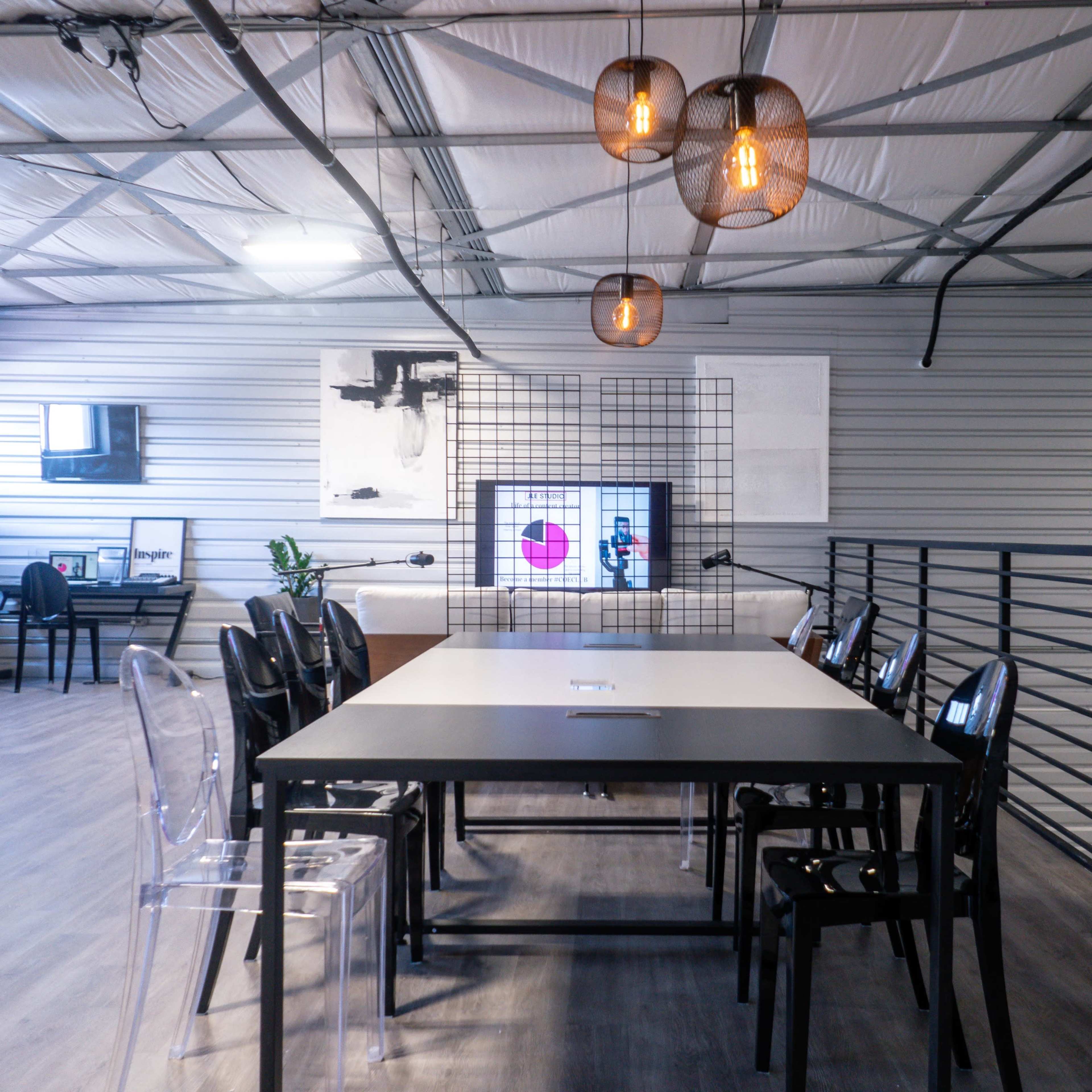 A modern meeting space with a large table, clear plastic chairs, and a wall display featuring a screen and decorative elements.