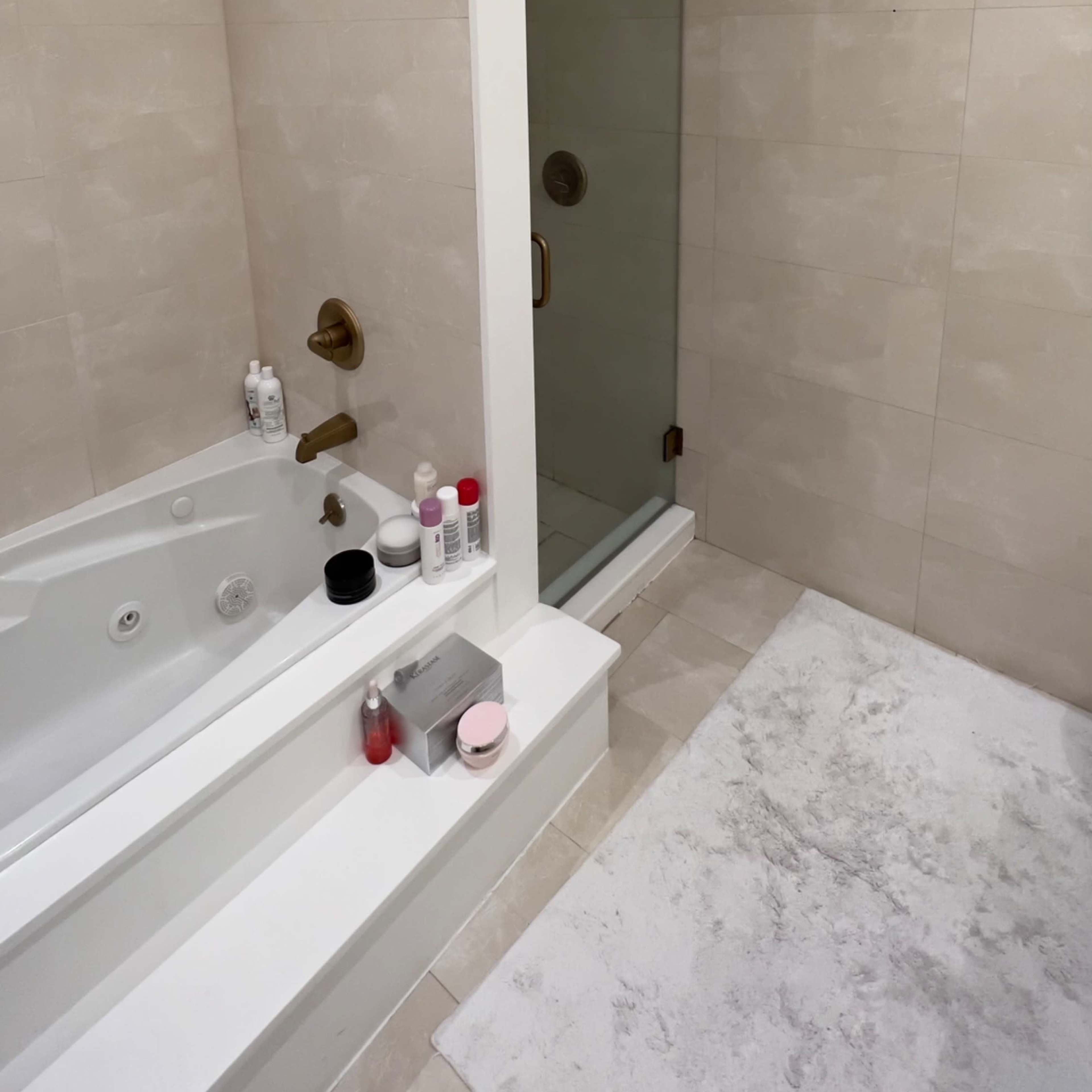 A modern bathroom featuring a bathtub with a shower, a glass shower enclosure, and light-colored tiled walls.