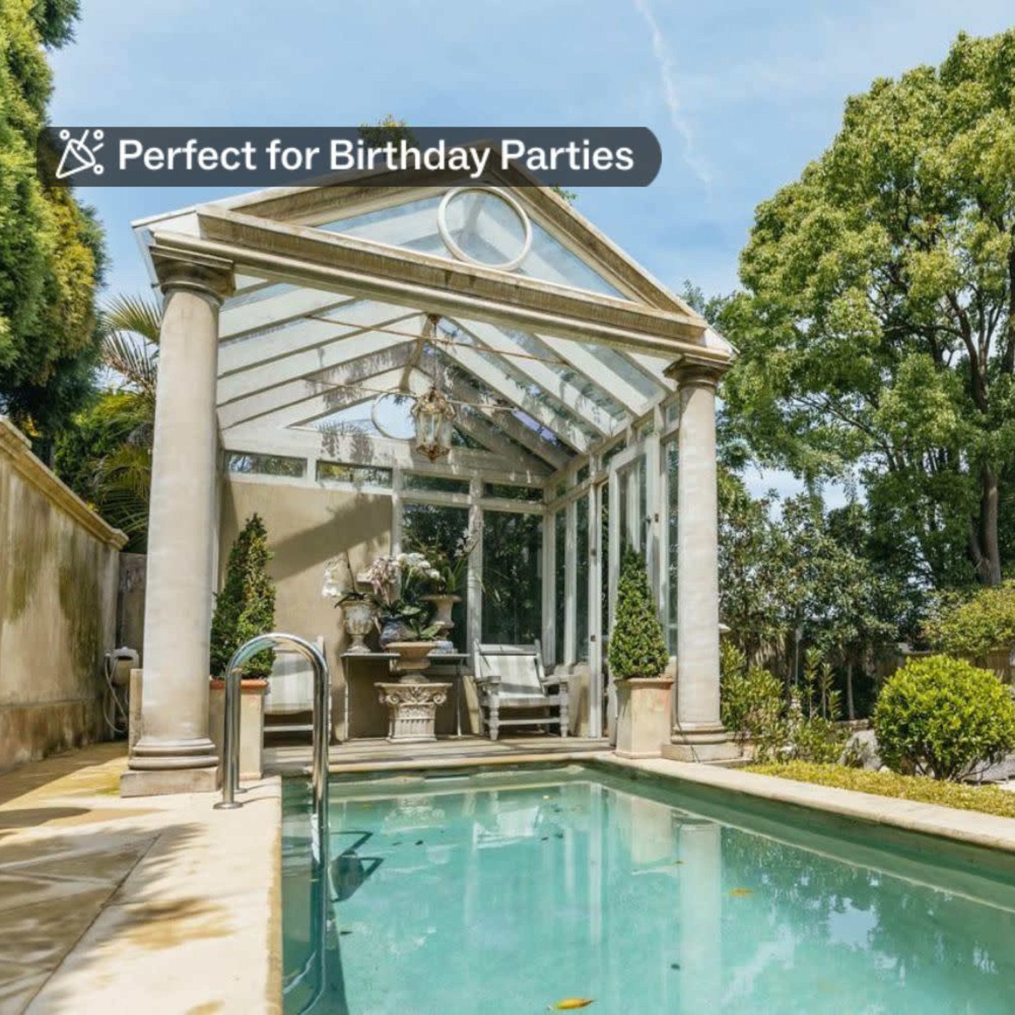 A glass-enclosed structure near a pool is surrounded by greenery and decorative plants.