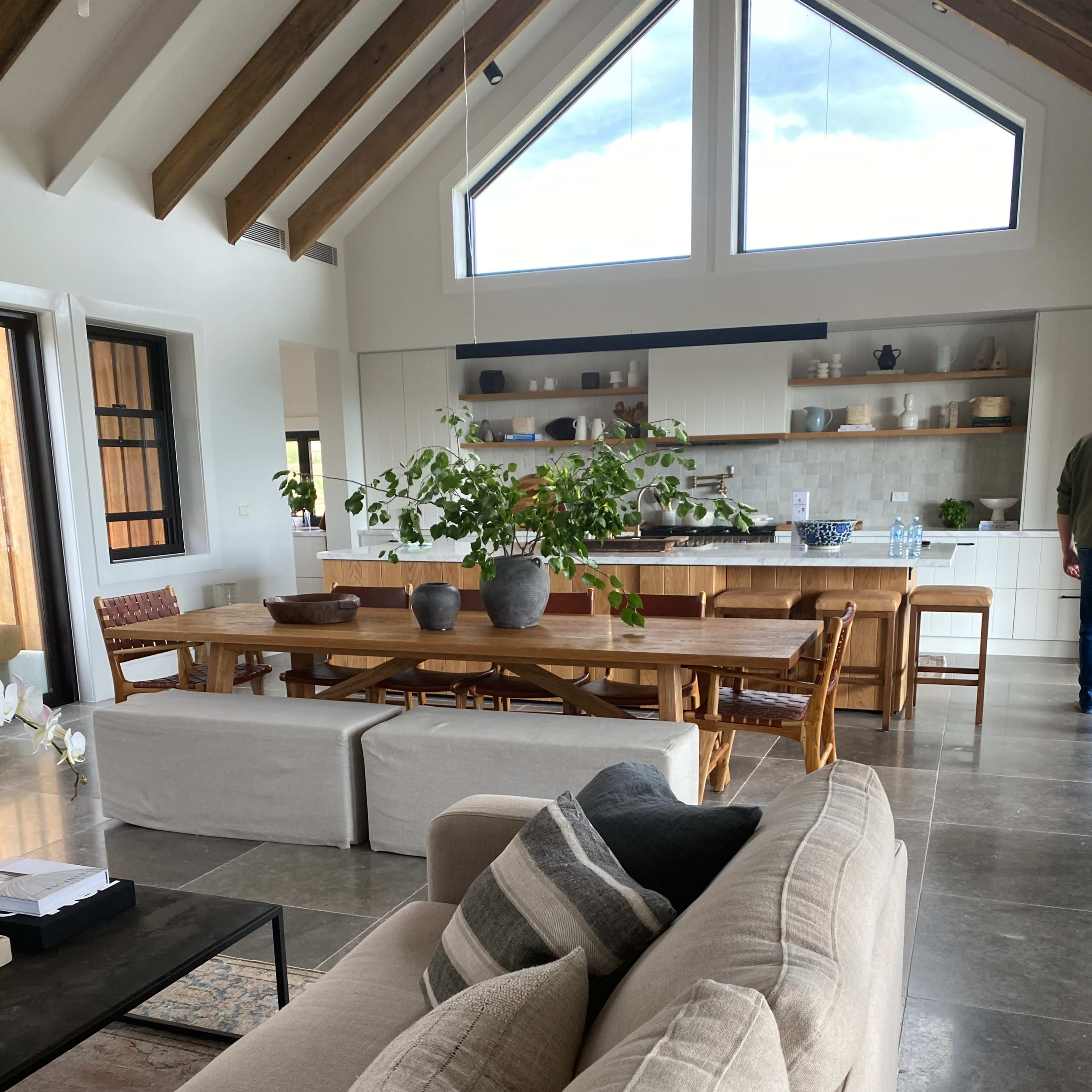 A spacious living area with a large kitchen and dining table, featuring high ceilings and multiple large windows.