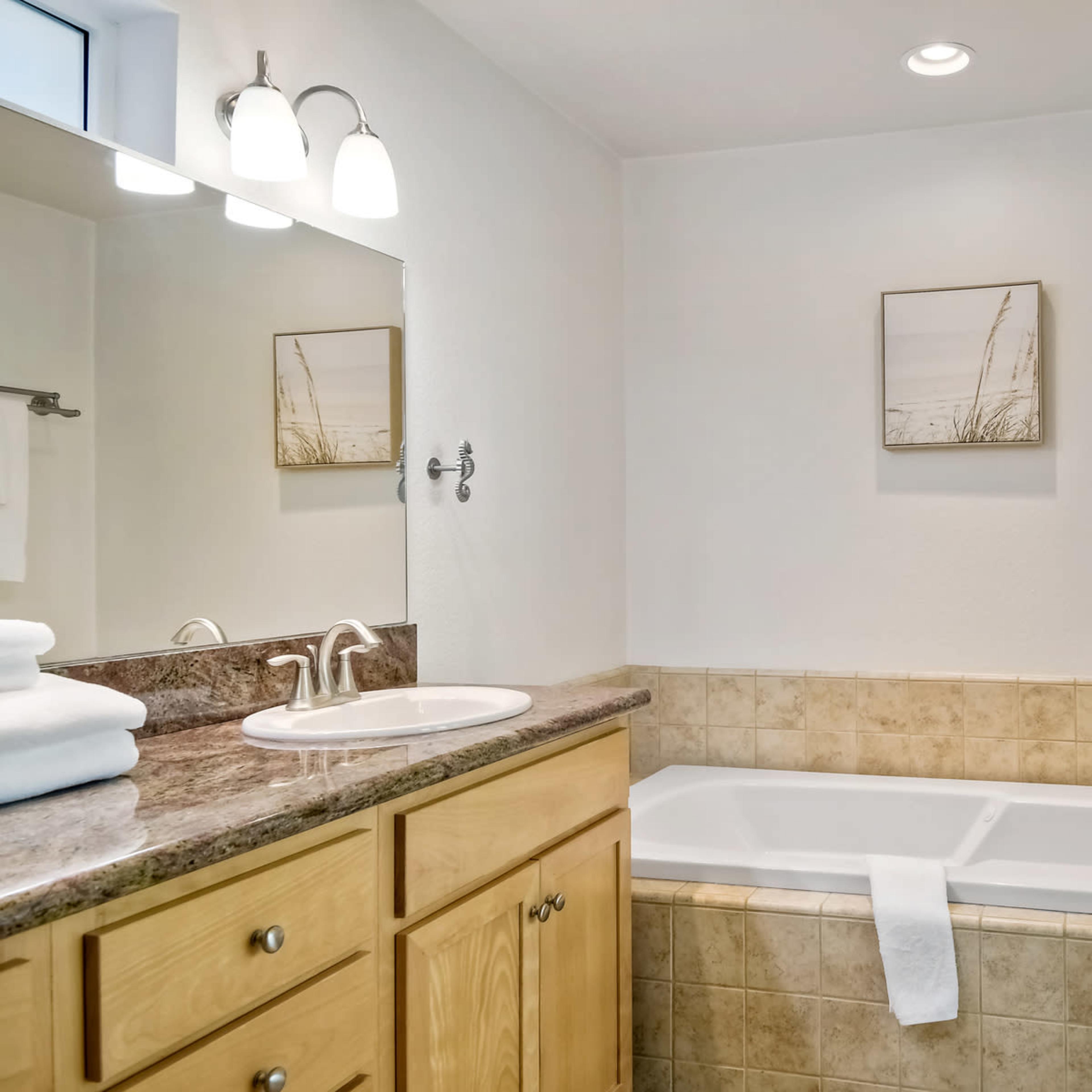 A bathroom featuring a tub, a sink with wooden cabinetry, and light-colored walls with decorative artwork.