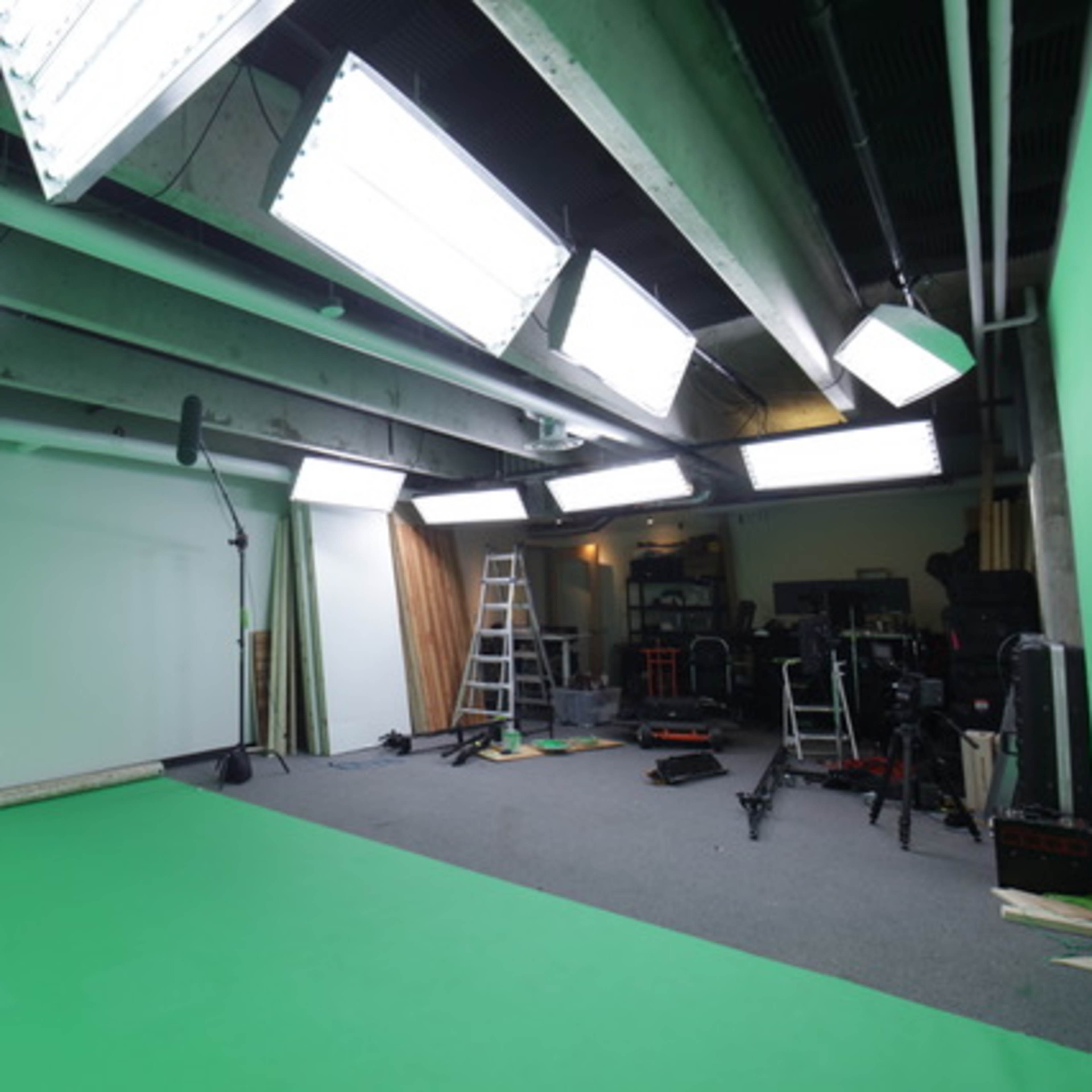 A green screen studio is equipped with bright lights, a ladder, and various camera equipment.