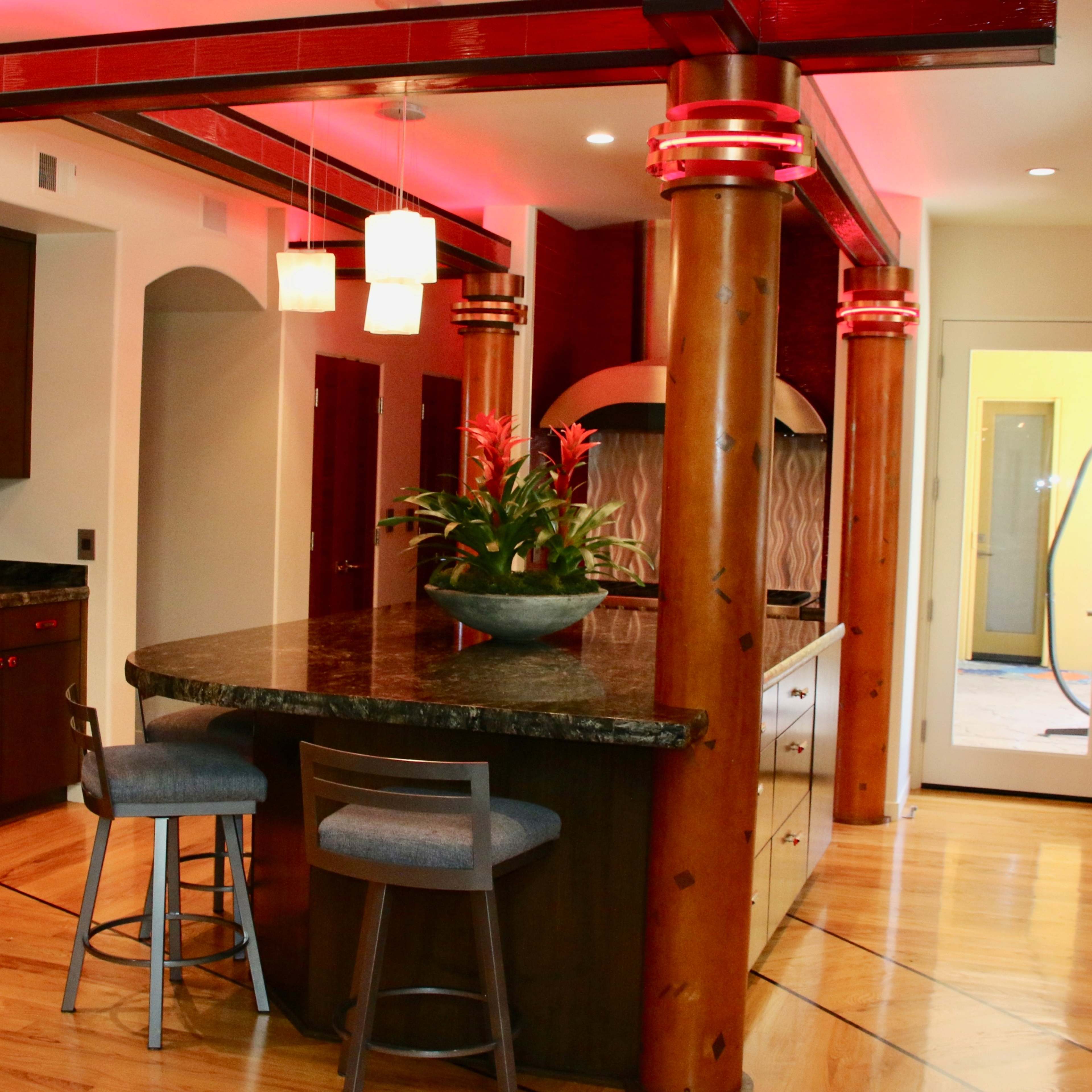 A modern kitchen with a large island, wooden pillars, and pendant lighting, featuring dark cabinetry and a granite countertop.