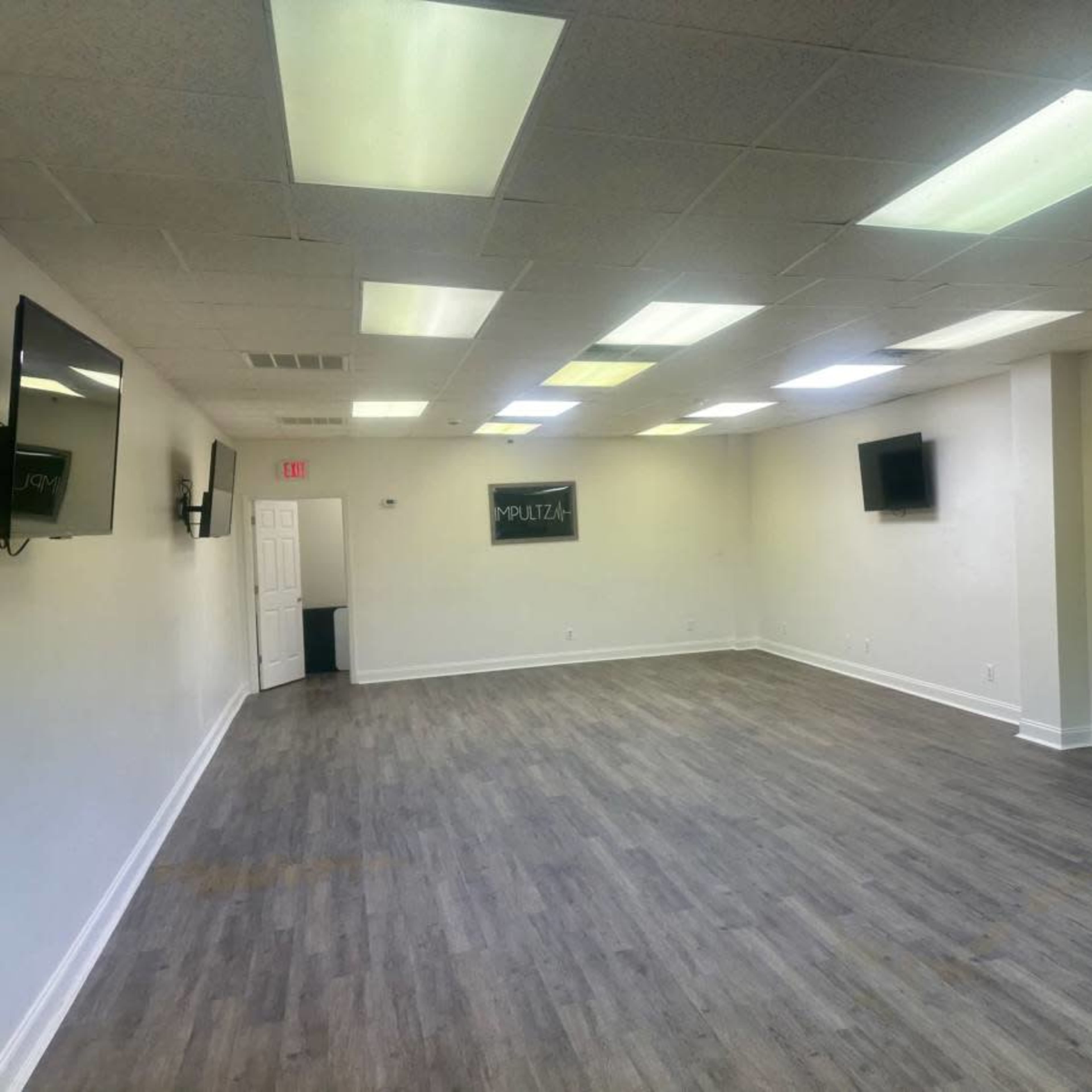 An empty room with vinyl flooring, white walls, and multiple flat-screen TVs mounted on the walls.
