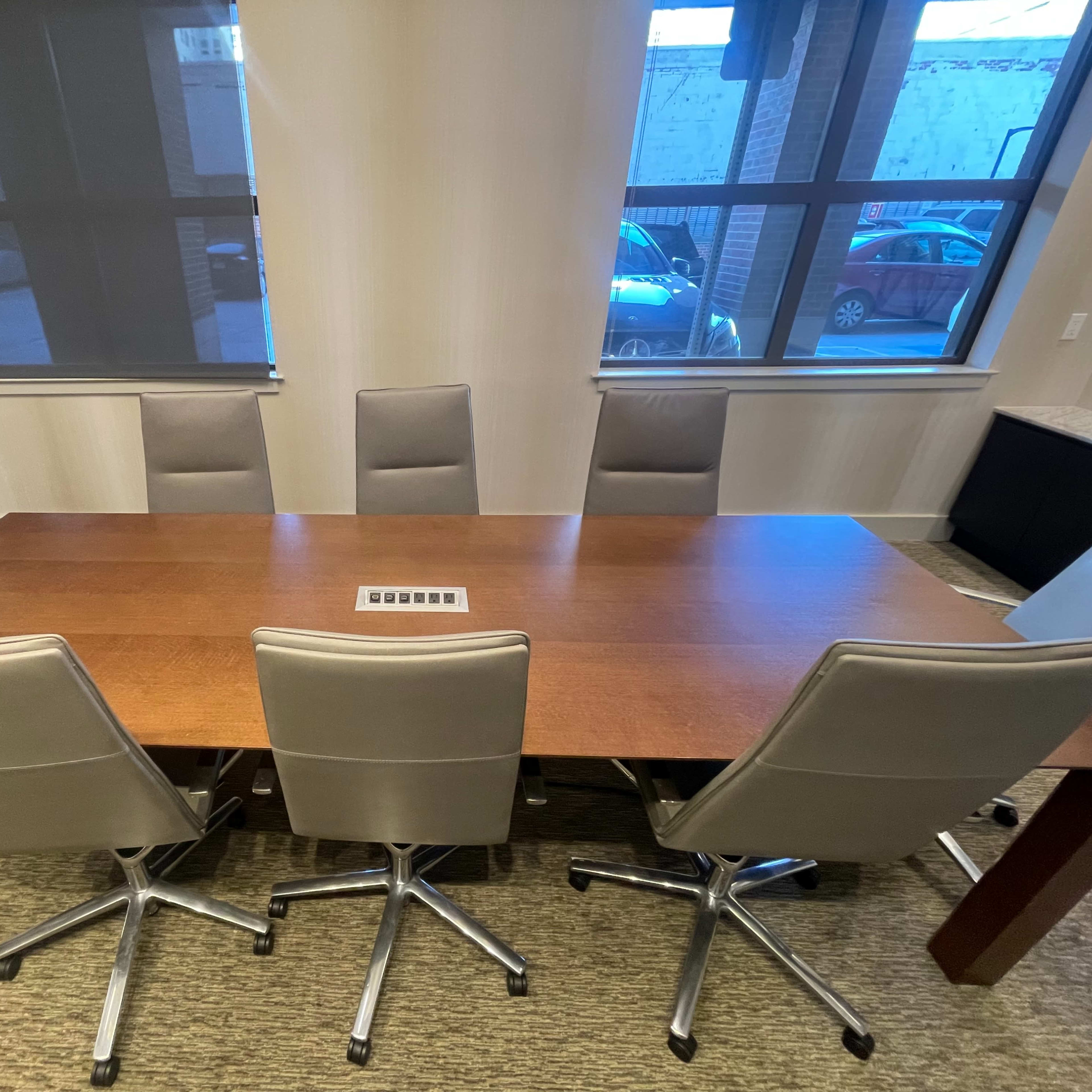 A large wooden conference table is surrounded by eight modern swivel chairs in a well-lit meeting room.