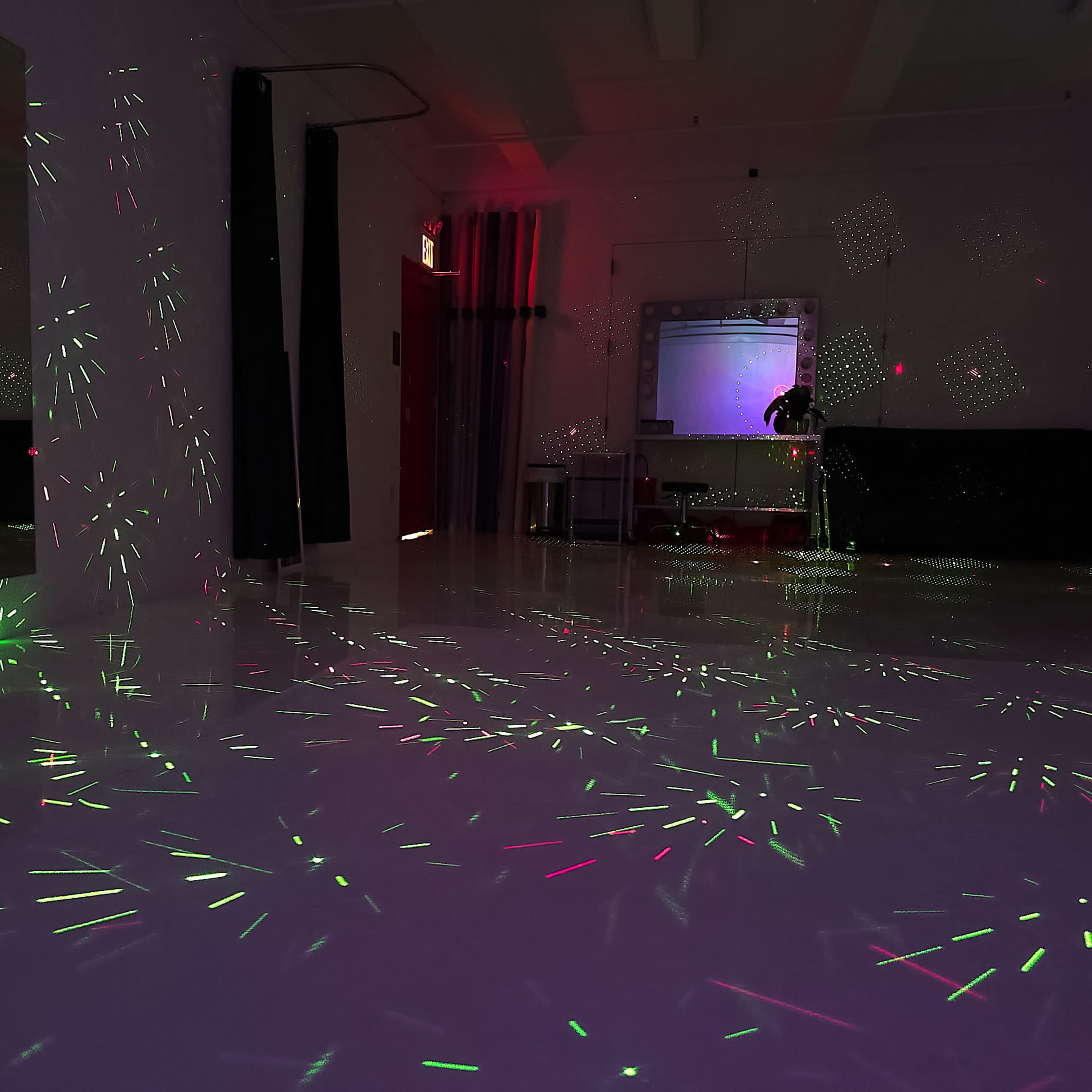 A room with a reflective floor illuminated by green and red light patterns.