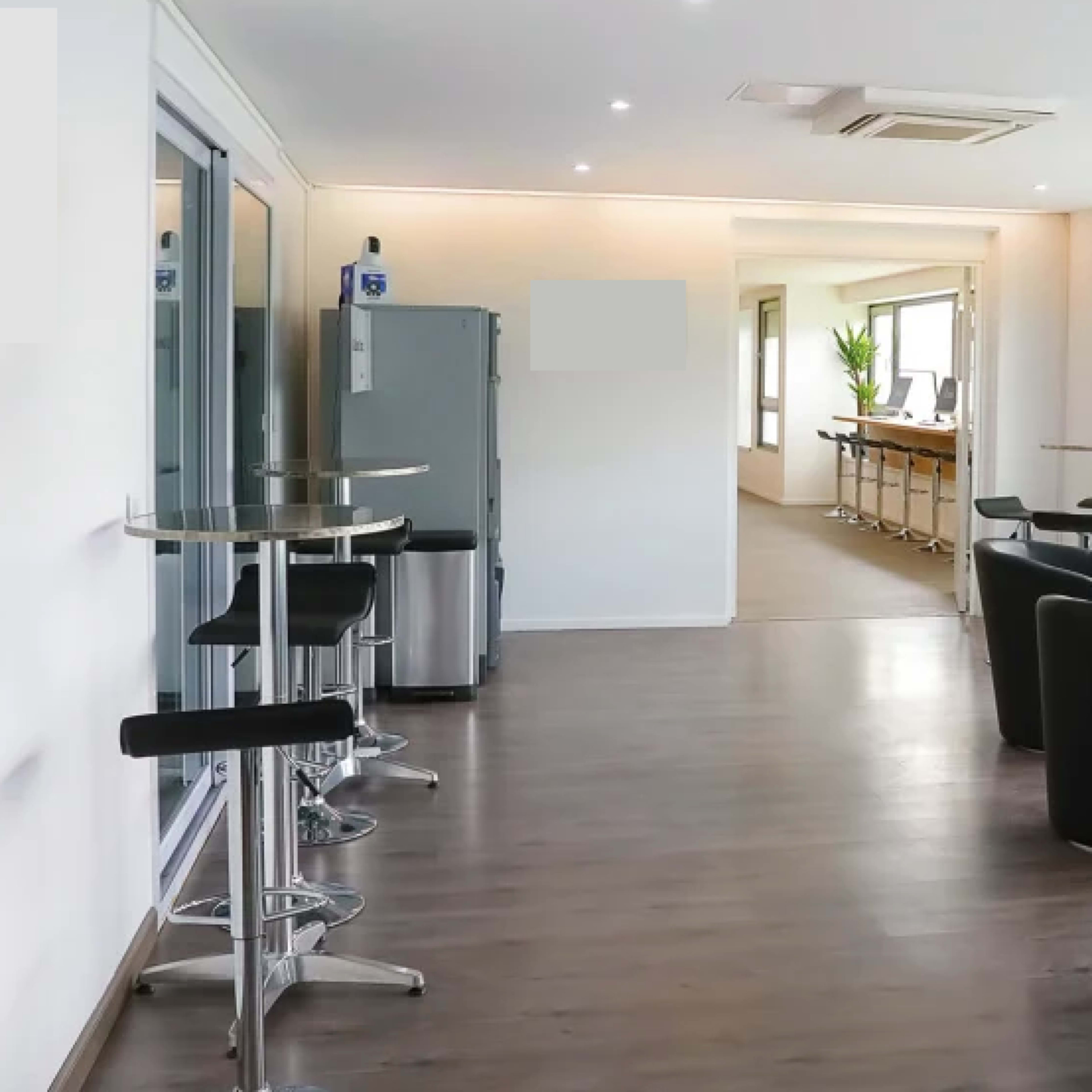 A modern indoor space with a bar area, seating arrangements of black chairs, and large windows allowing natural light.