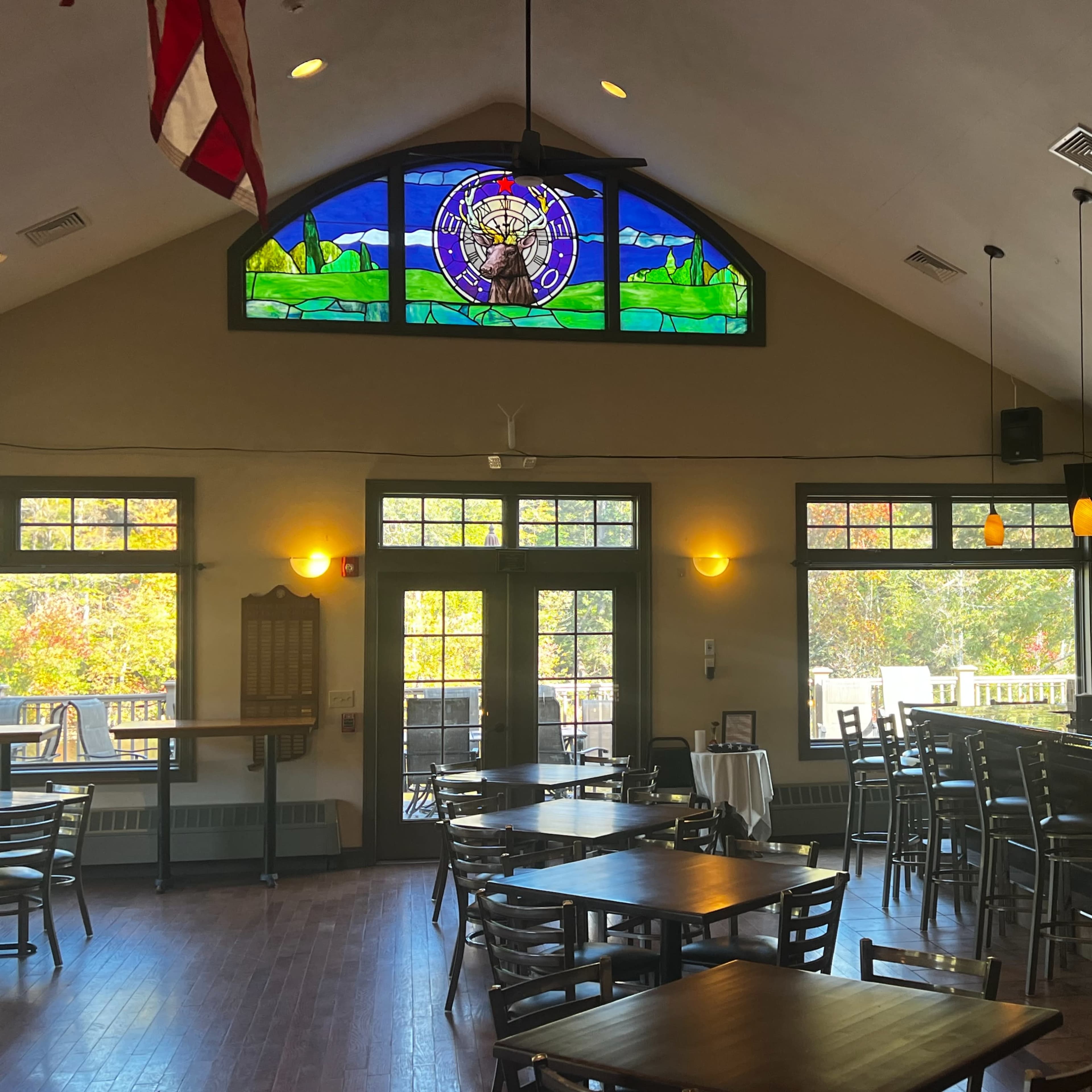 A well-lit interior of a restaurant or bar featuring wooden tables, a bar counter, and large windows with a stained glass design.