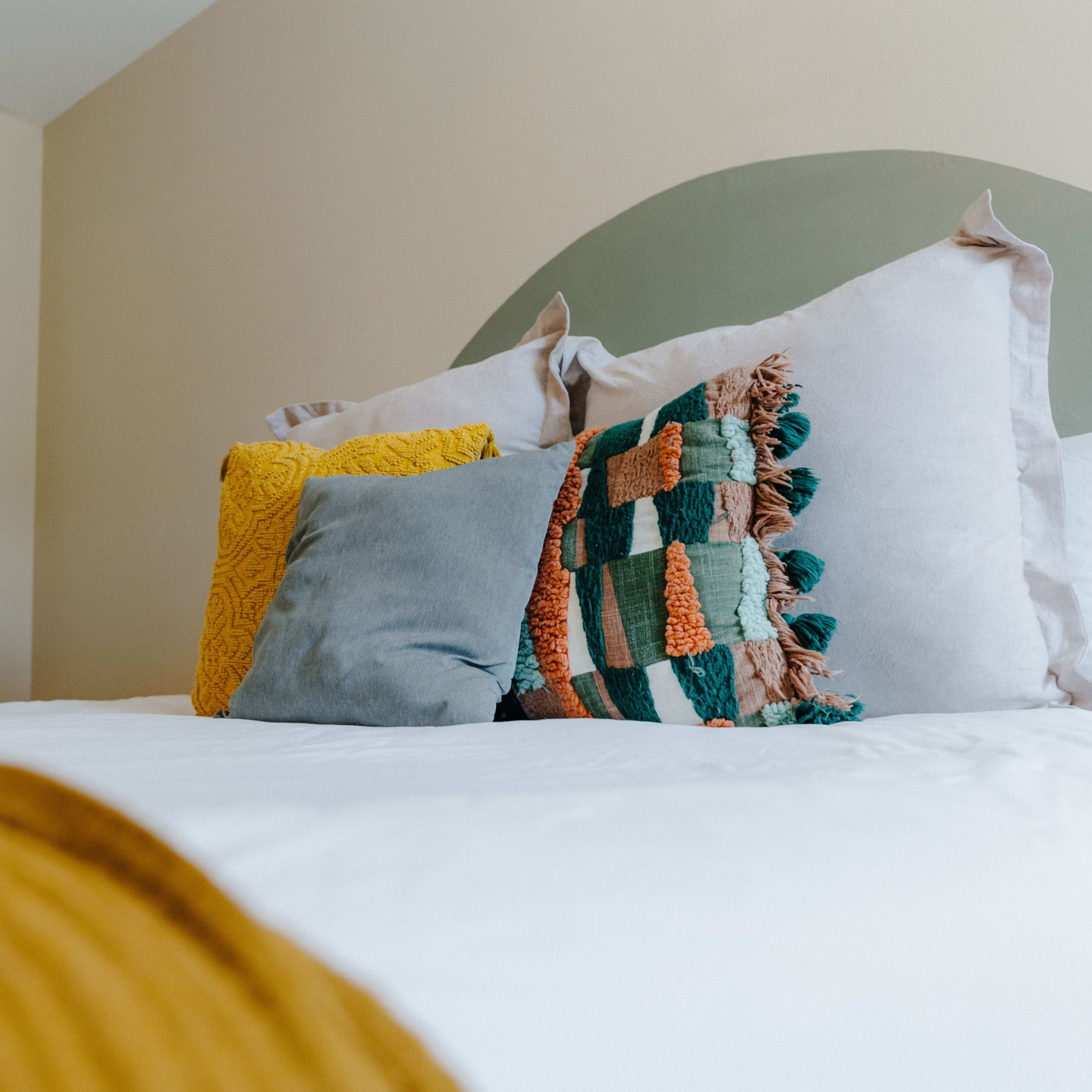 A neatly made bed with decorative pillows is positioned against a light-colored wall, featuring a closed door in the background.