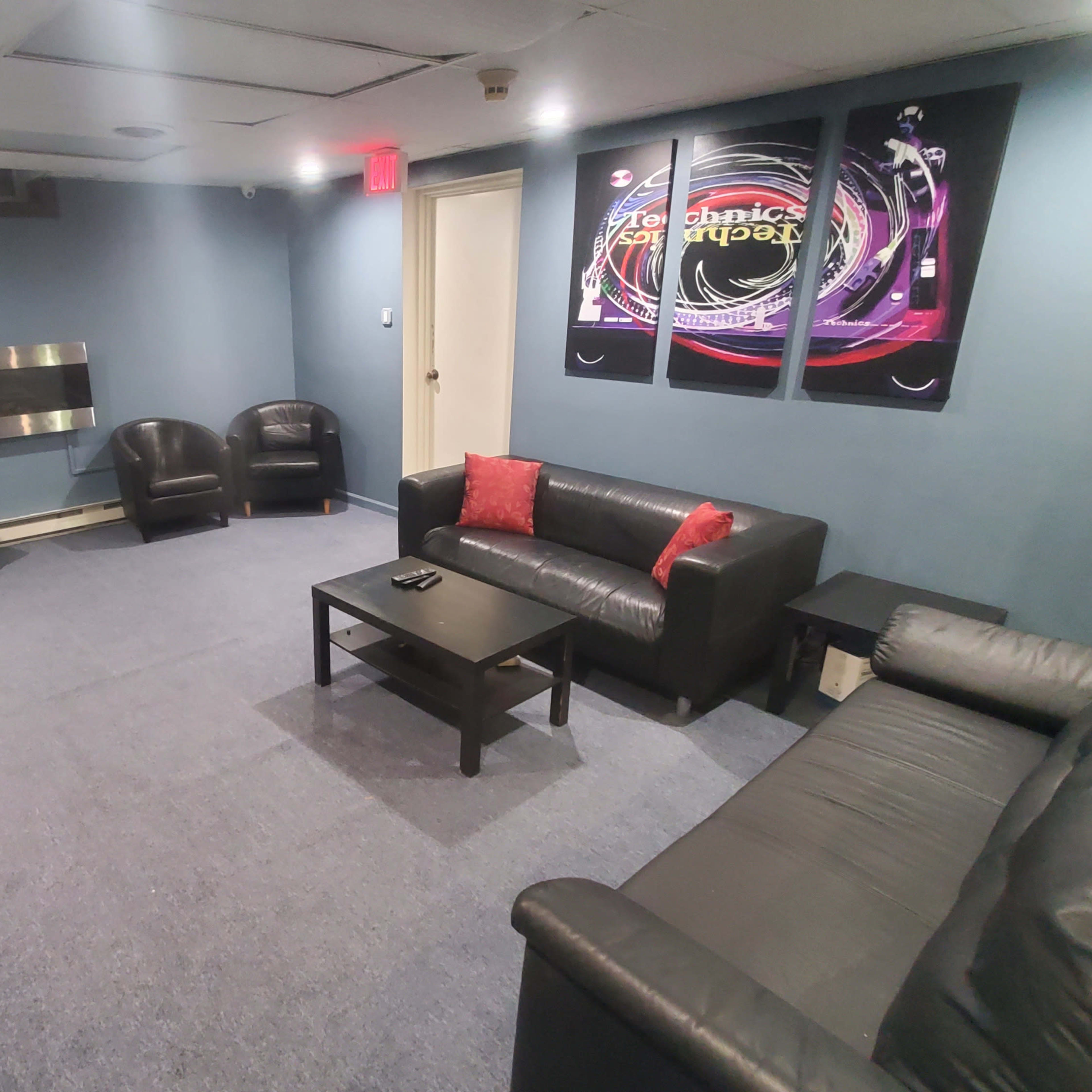 A small lounge area with two black leather sofas, two armchairs, a coffee table, and wall-mounted artwork.