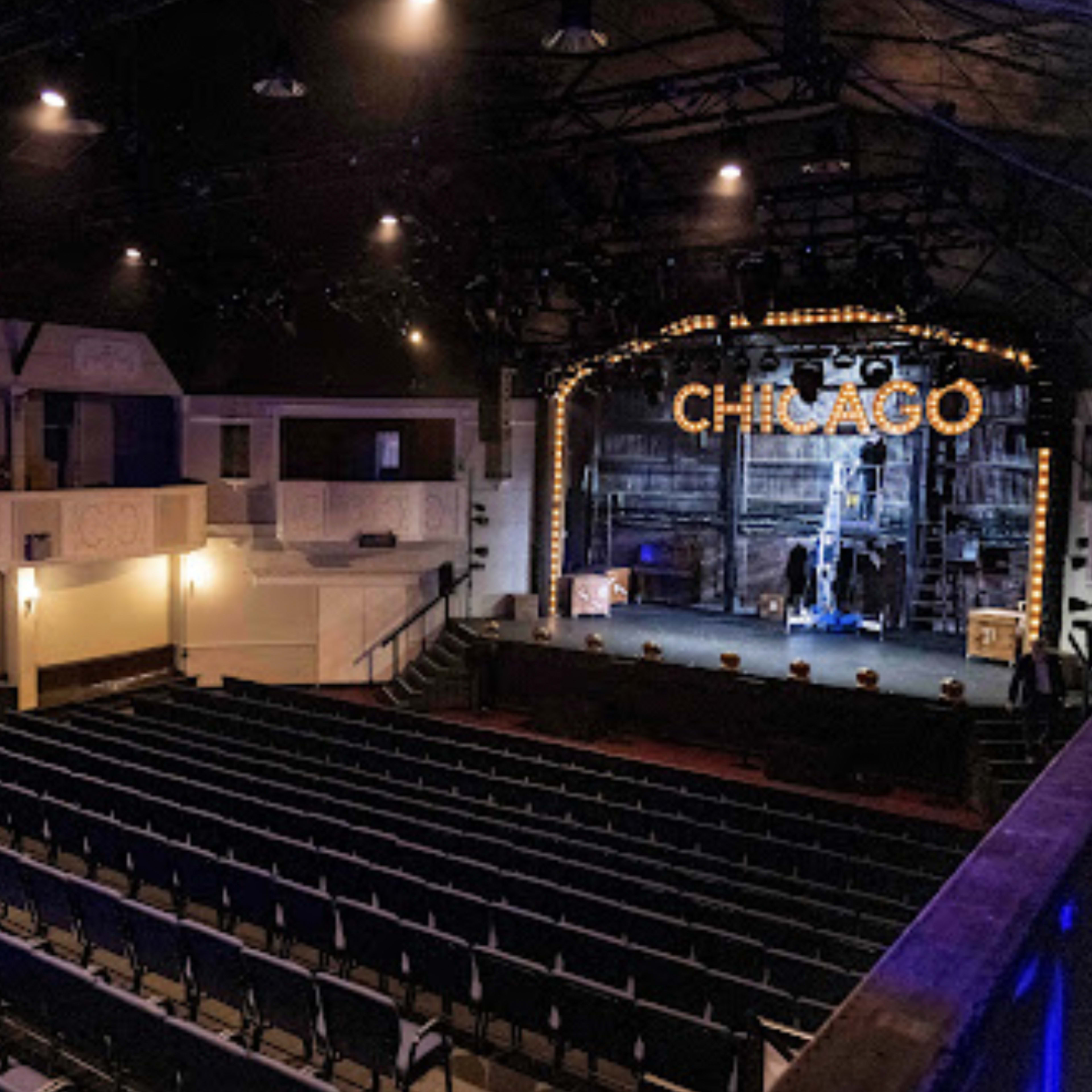 An empty theater with a stage labeled "CHICAGO," featuring rows of seats and a variety of stage lighting.