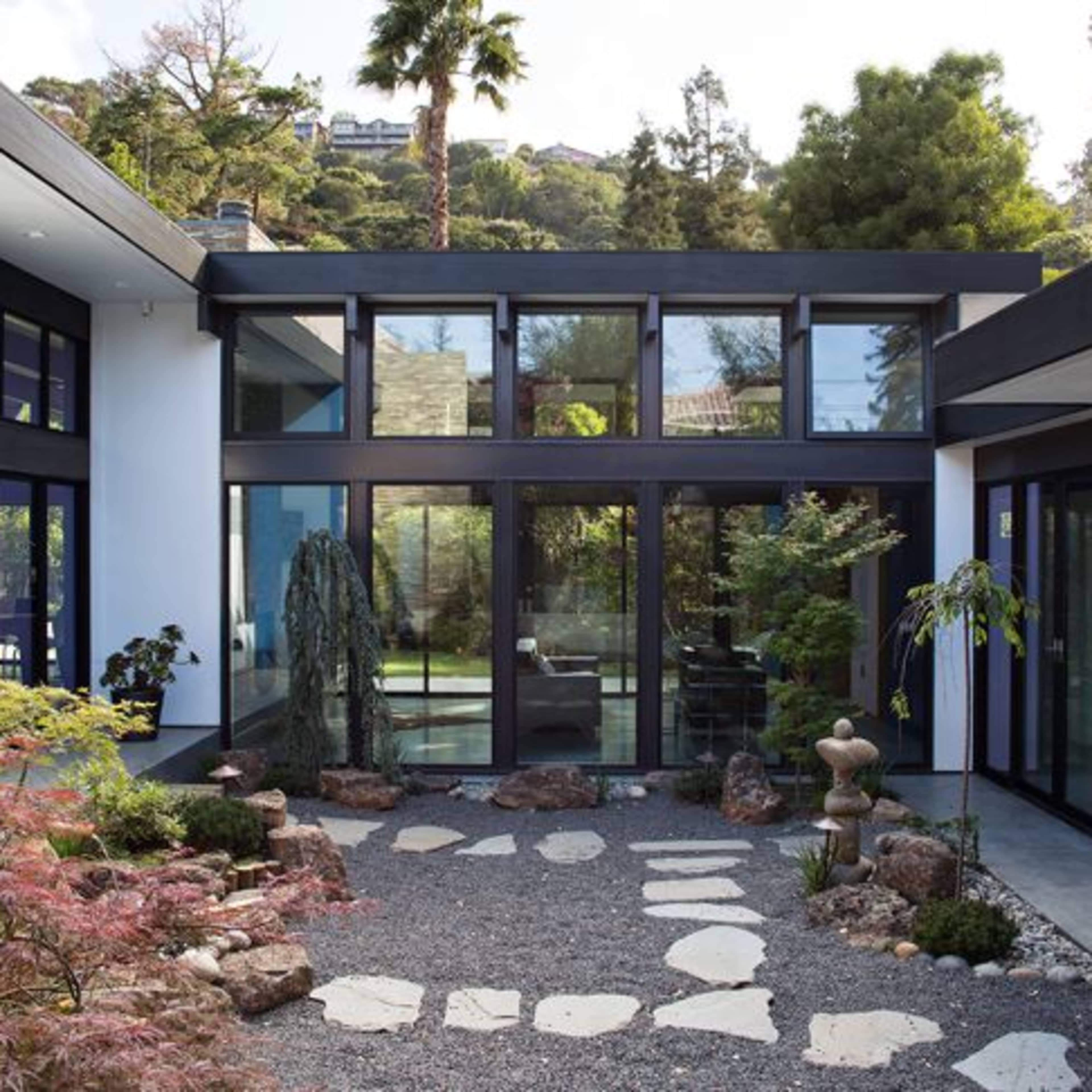 A modern courtyard surrounded by sleek glass walls, featuring a gravel path and landscaped plants.