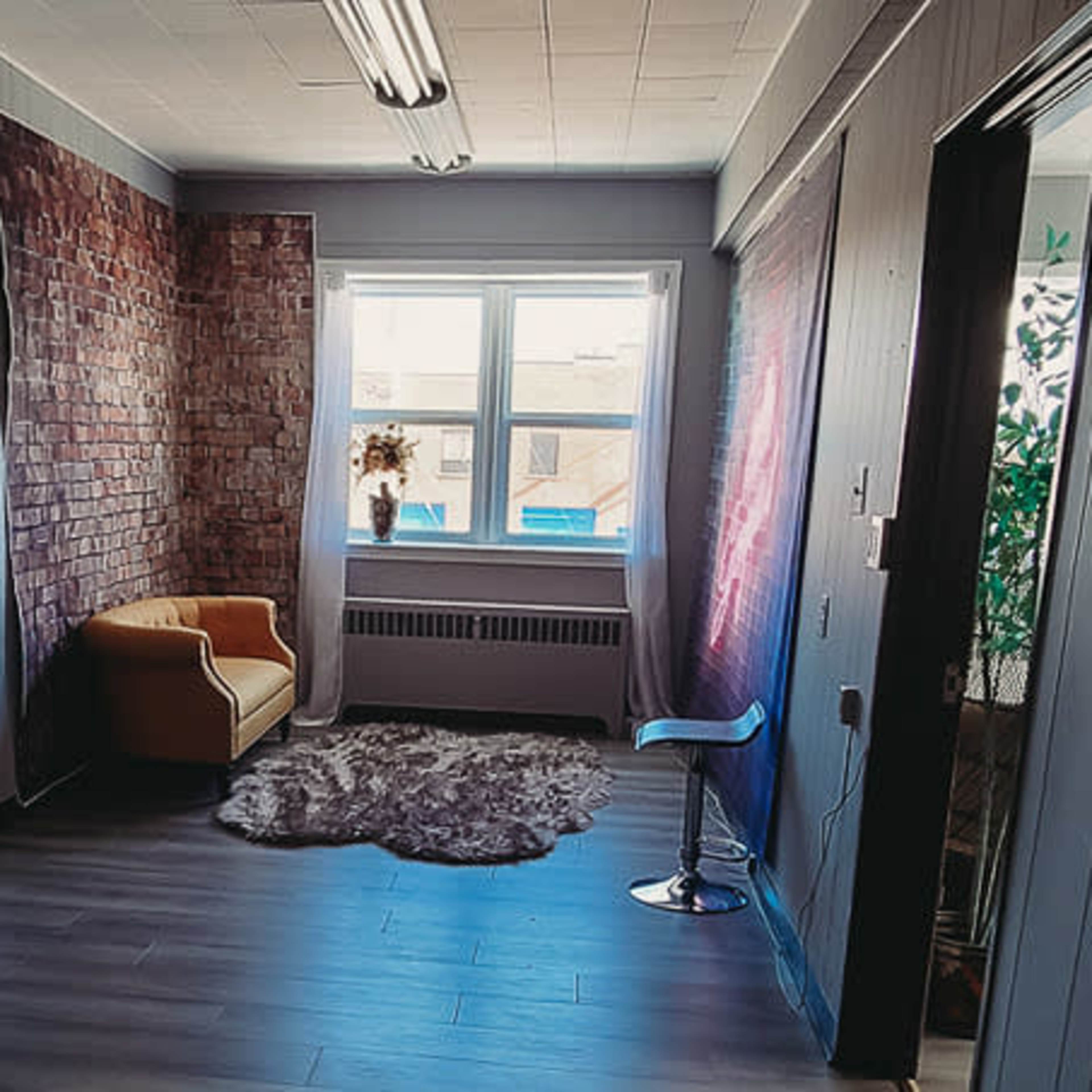 A hallway with a brick feature wall, a yellow armchair, and a window facing the outside.