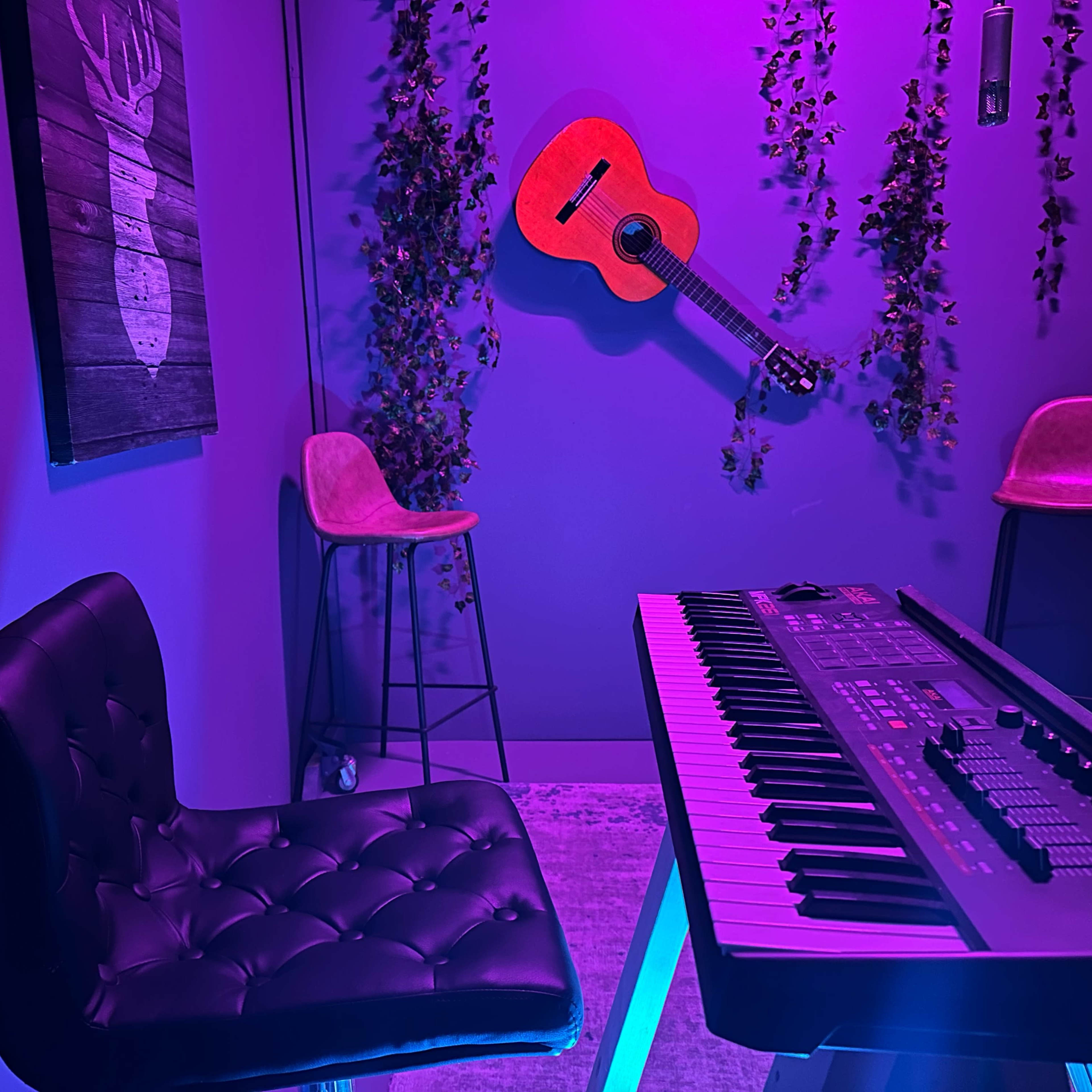 A dark purple room features a keyboard, a black chair, a hanging guitar, and two bar stools alongside a wall adorned with vines.