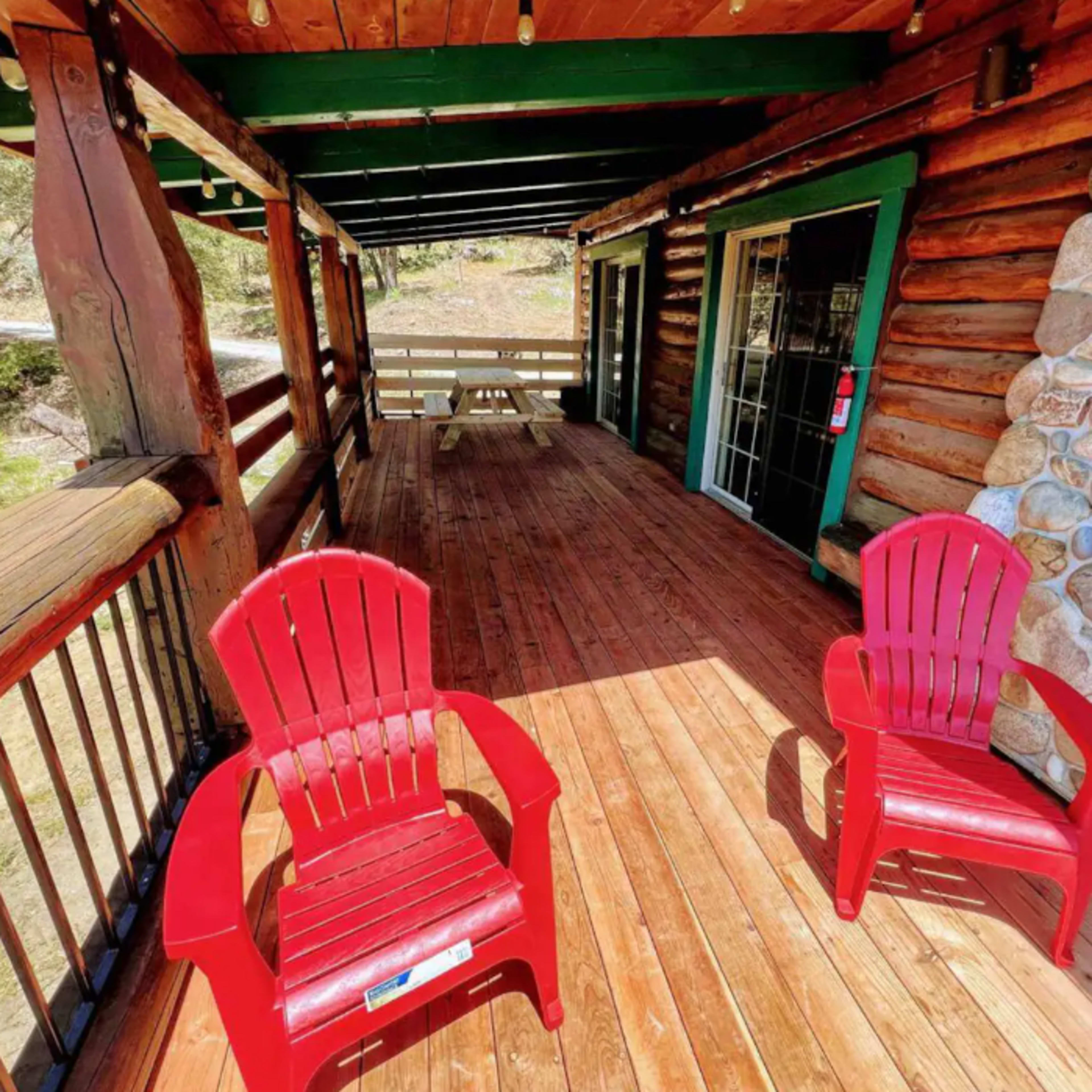 A wooden porch featuring two red chairs and a stone wall.