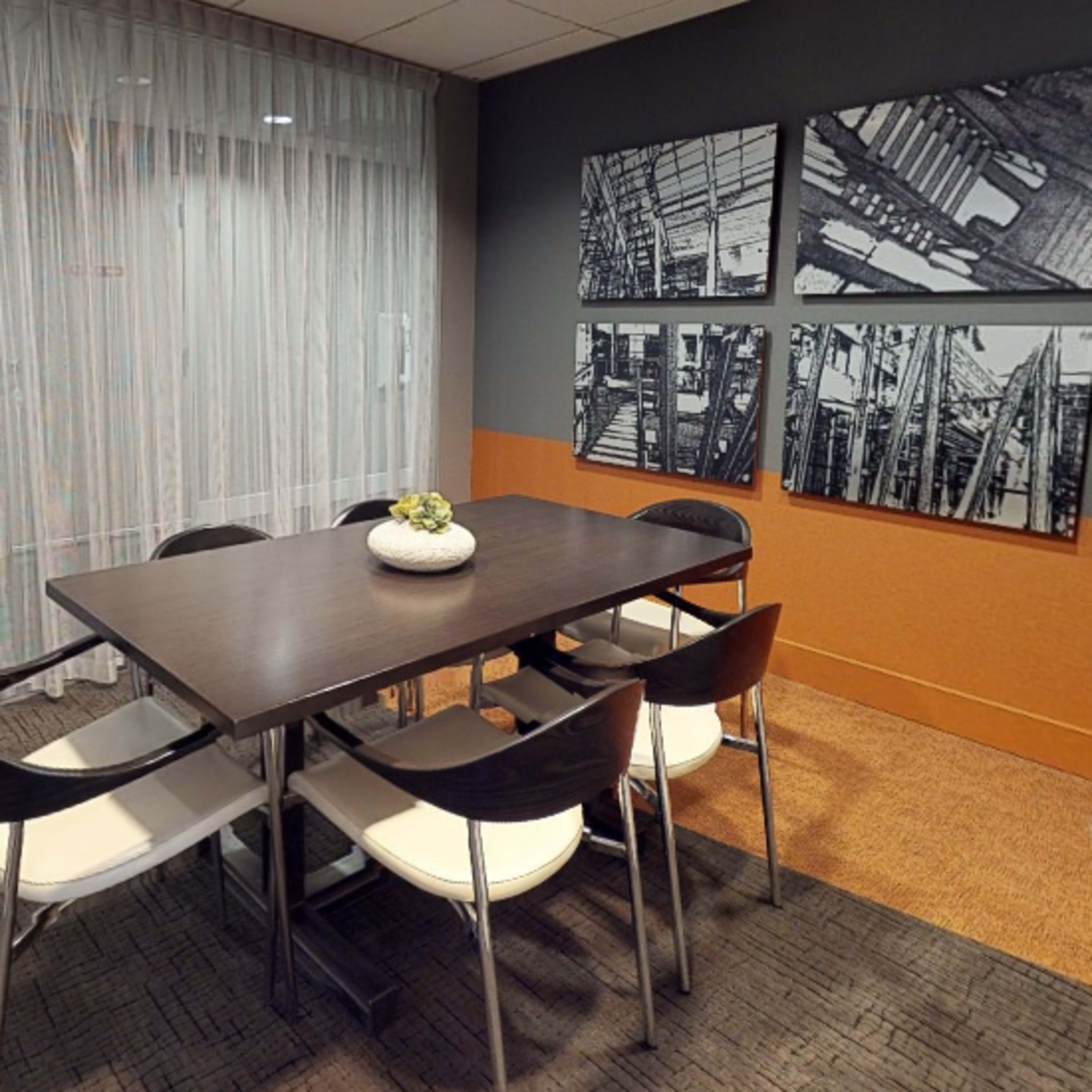A modern conference room features a rectangular table surrounded by six chairs and decorated with a potted plant, along with framed black-and-white photographs on the walls.