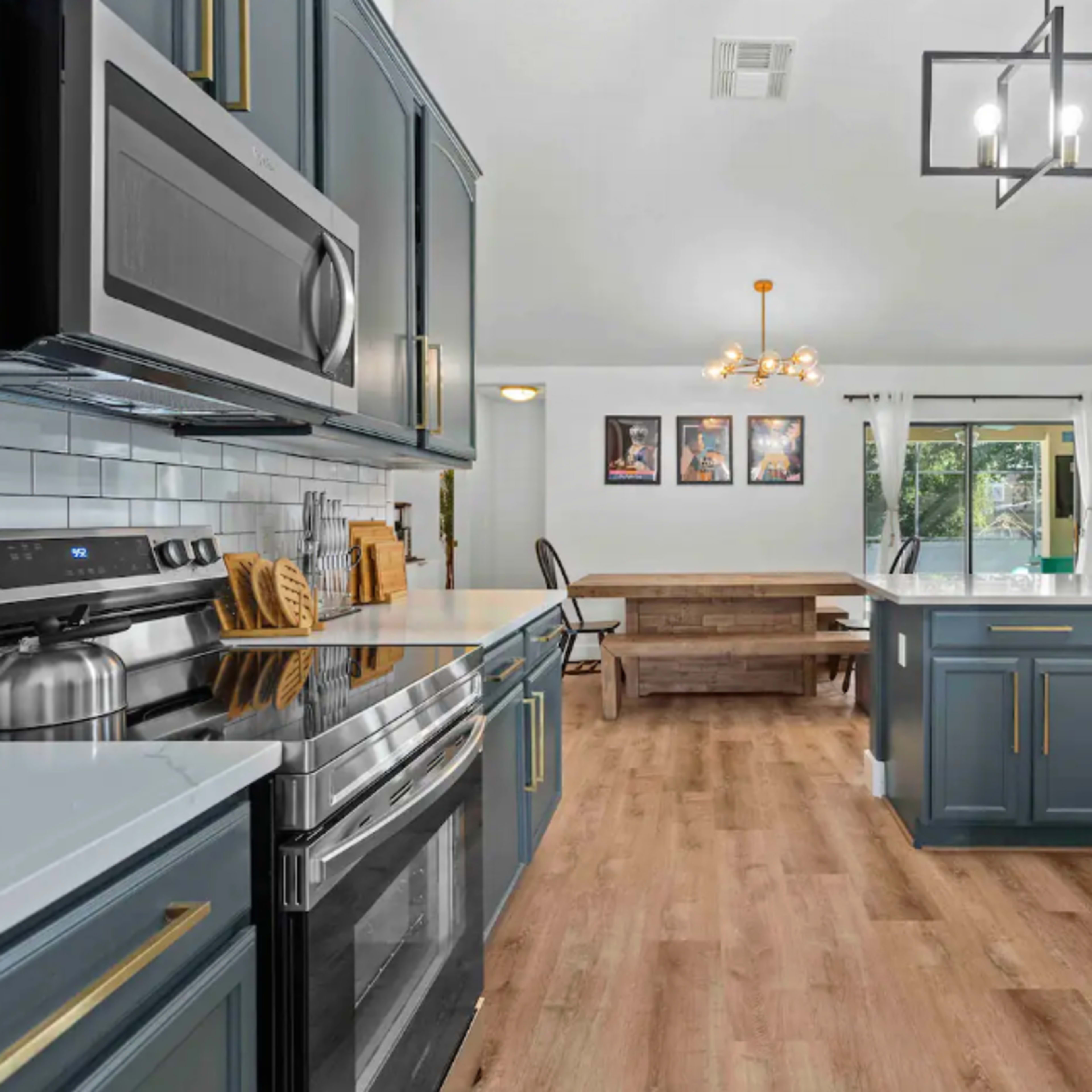 A modern kitchen features dark blue cabinetry, stainless steel appliances, and a dining area with a wooden table and chairs.