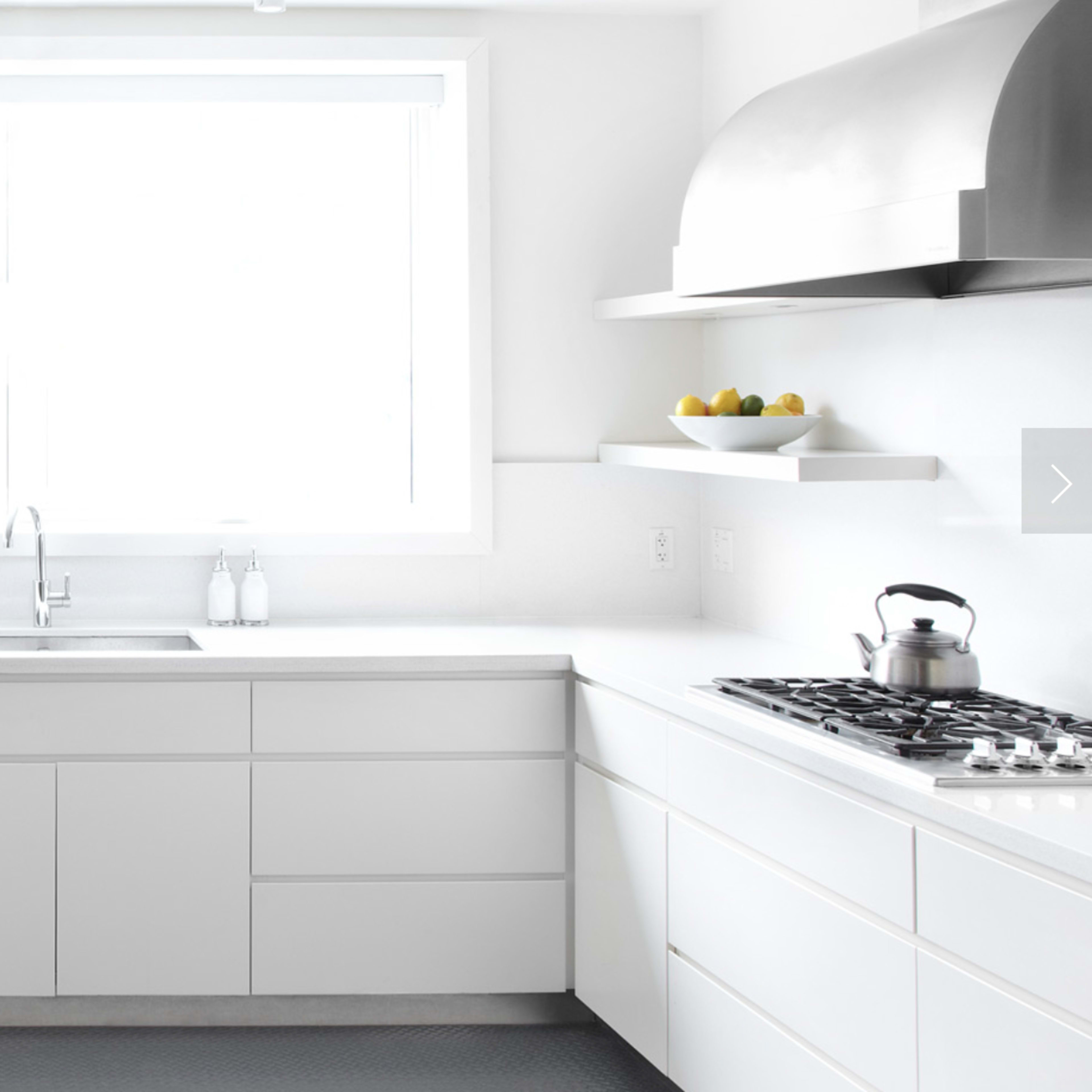 A modern kitchen features white cabinetry, a large window, stainless steel appliances, and a sleek countertop.