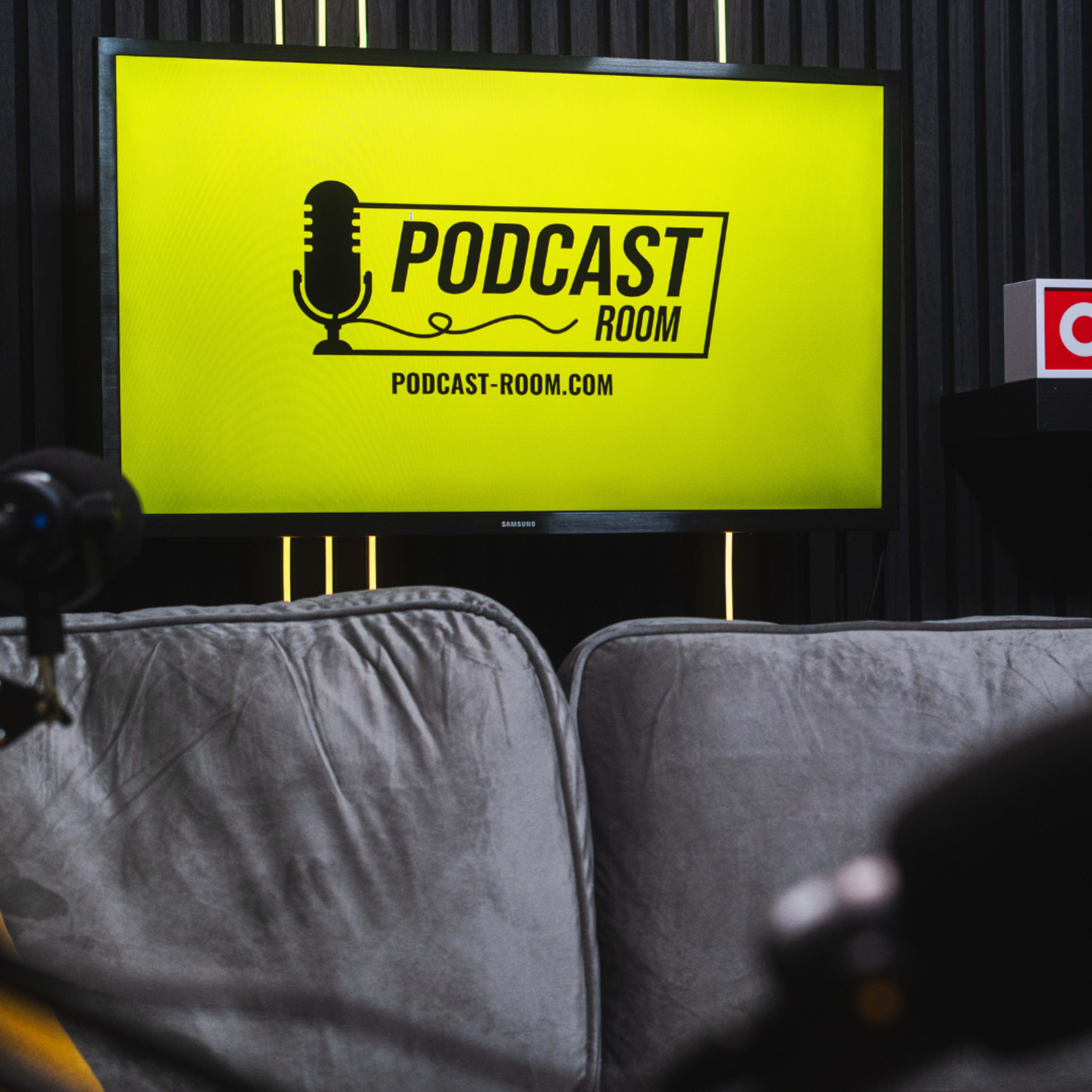 A television screen displaying a podcast logo and a "ON AIR" sign is set against a dark wooden backdrop, with microphones and a sofa in the foreground.