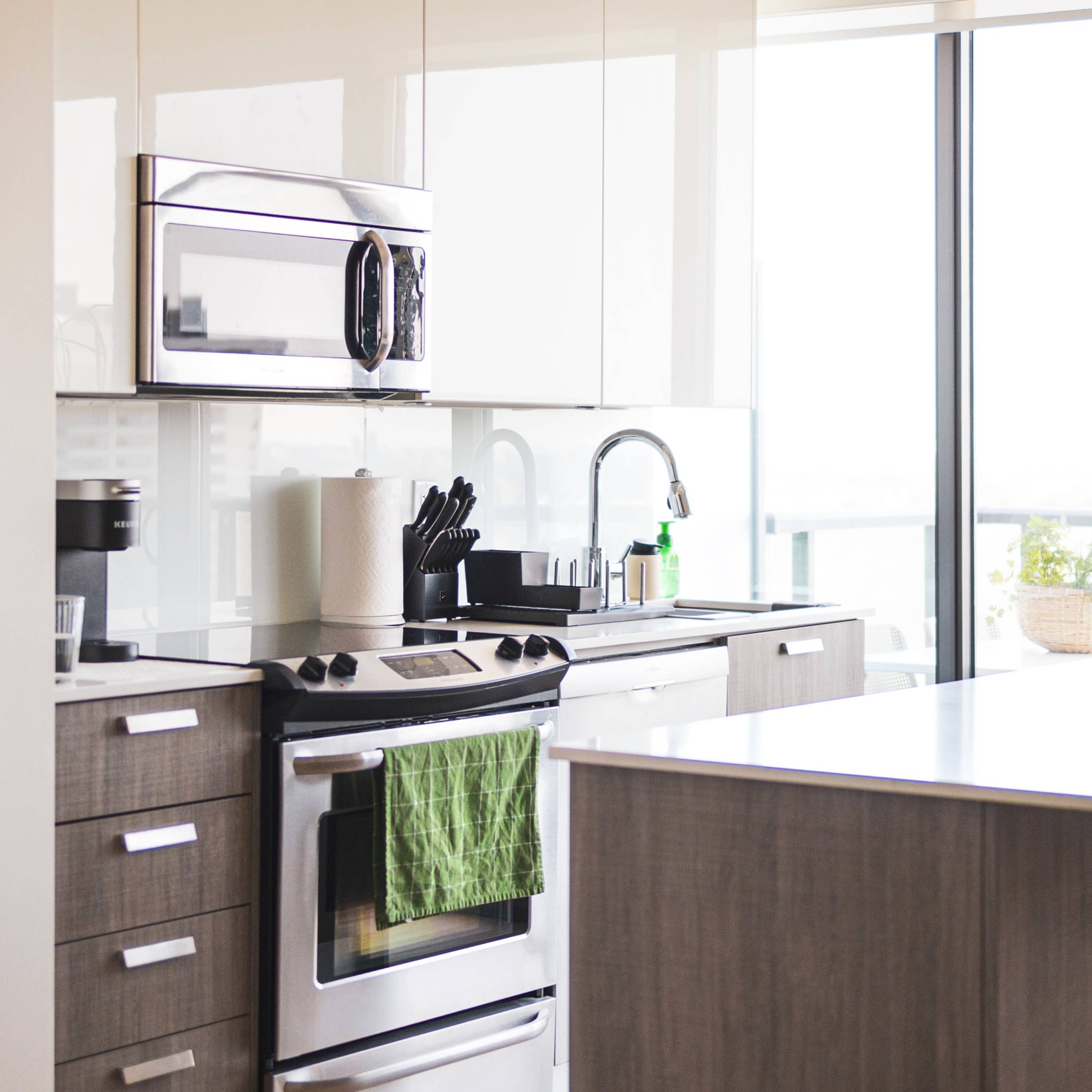 A modern kitchen with stainless steel appliances, a green dish towel hanging from the oven, and a large window providing natural light.