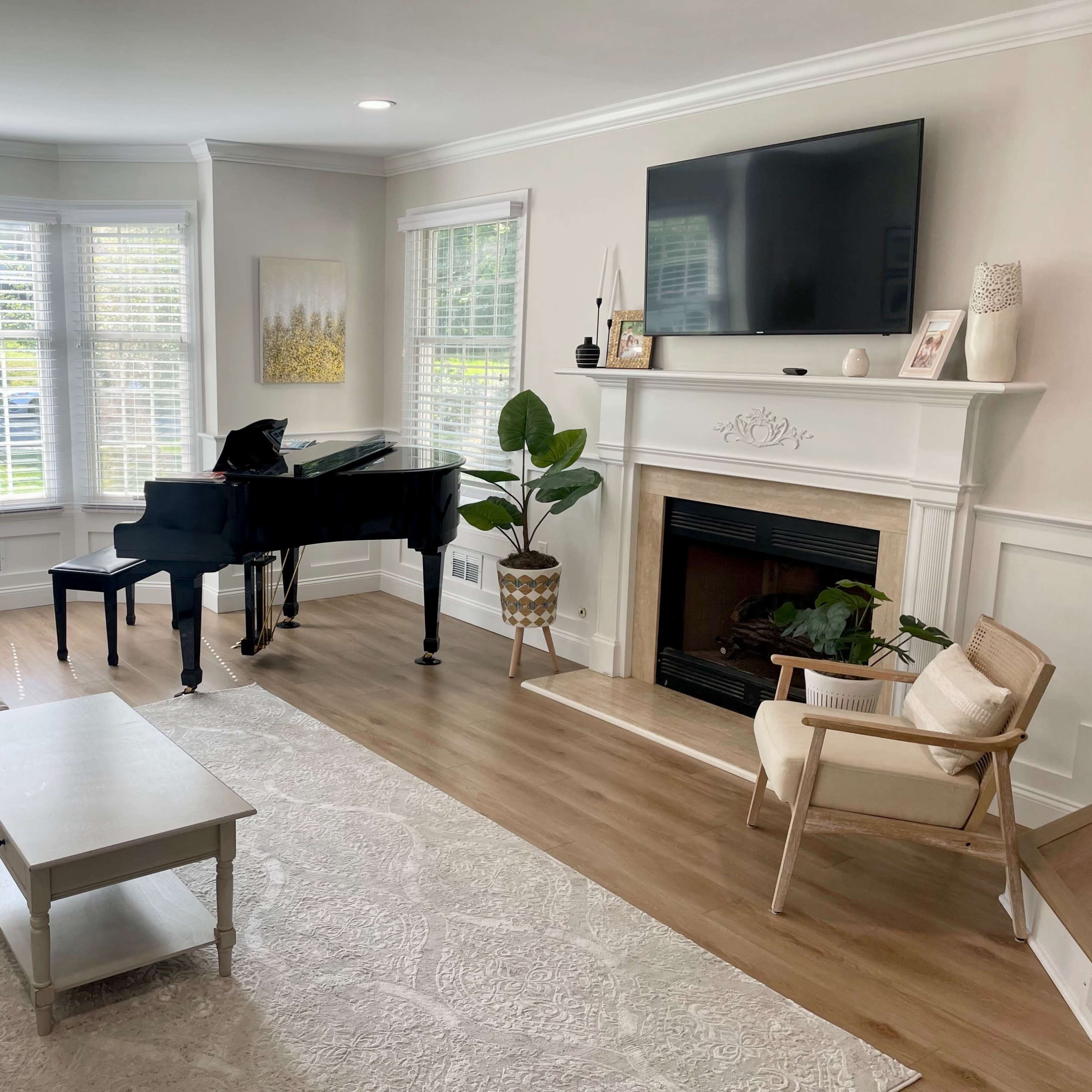 The living room features a black grand piano beside a beige sofa set, a coffee table, and a fireplace, with large windows allowing ample natural light.