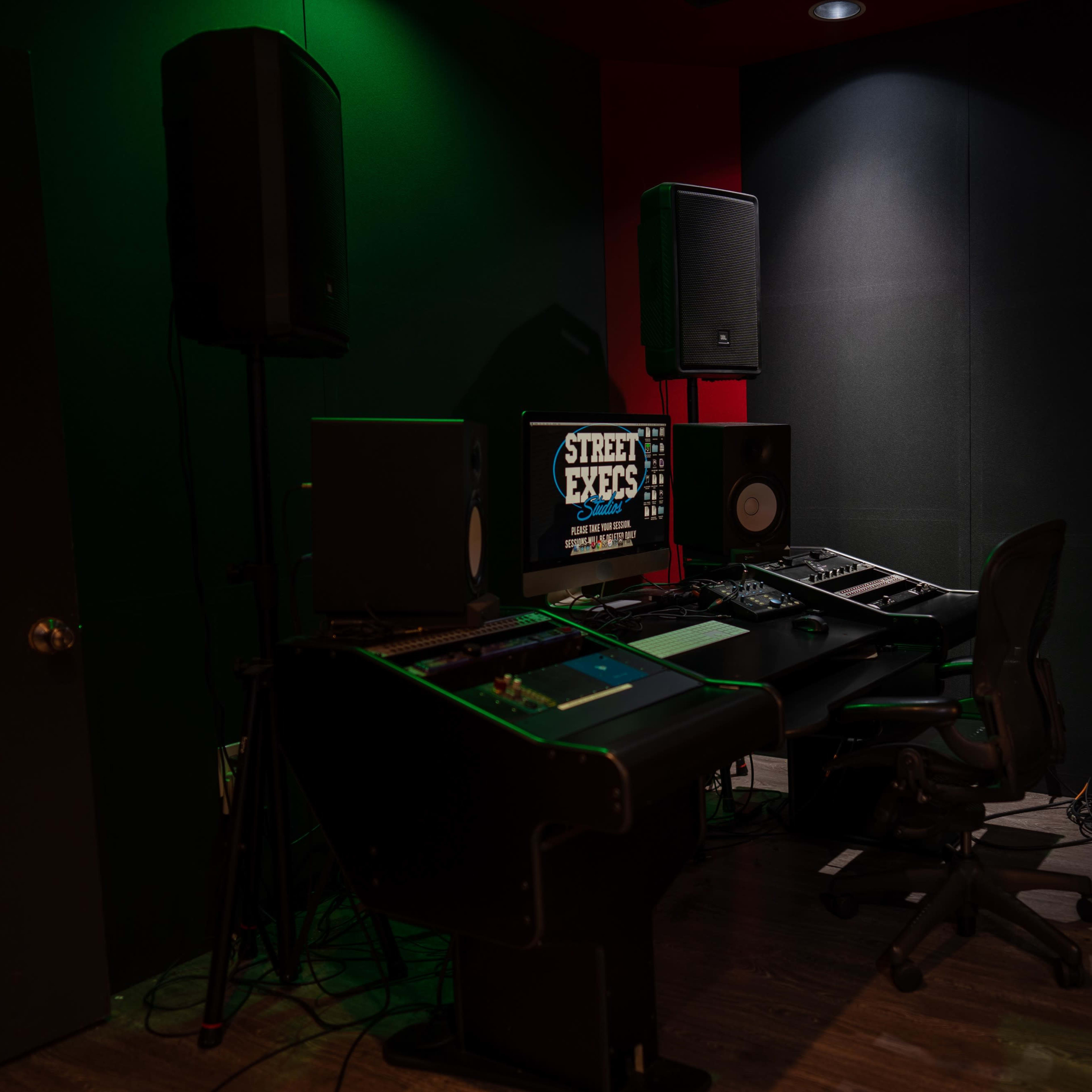 A music production studio featuring a desk with computer equipment, speakers, and soundproofing on the walls.
