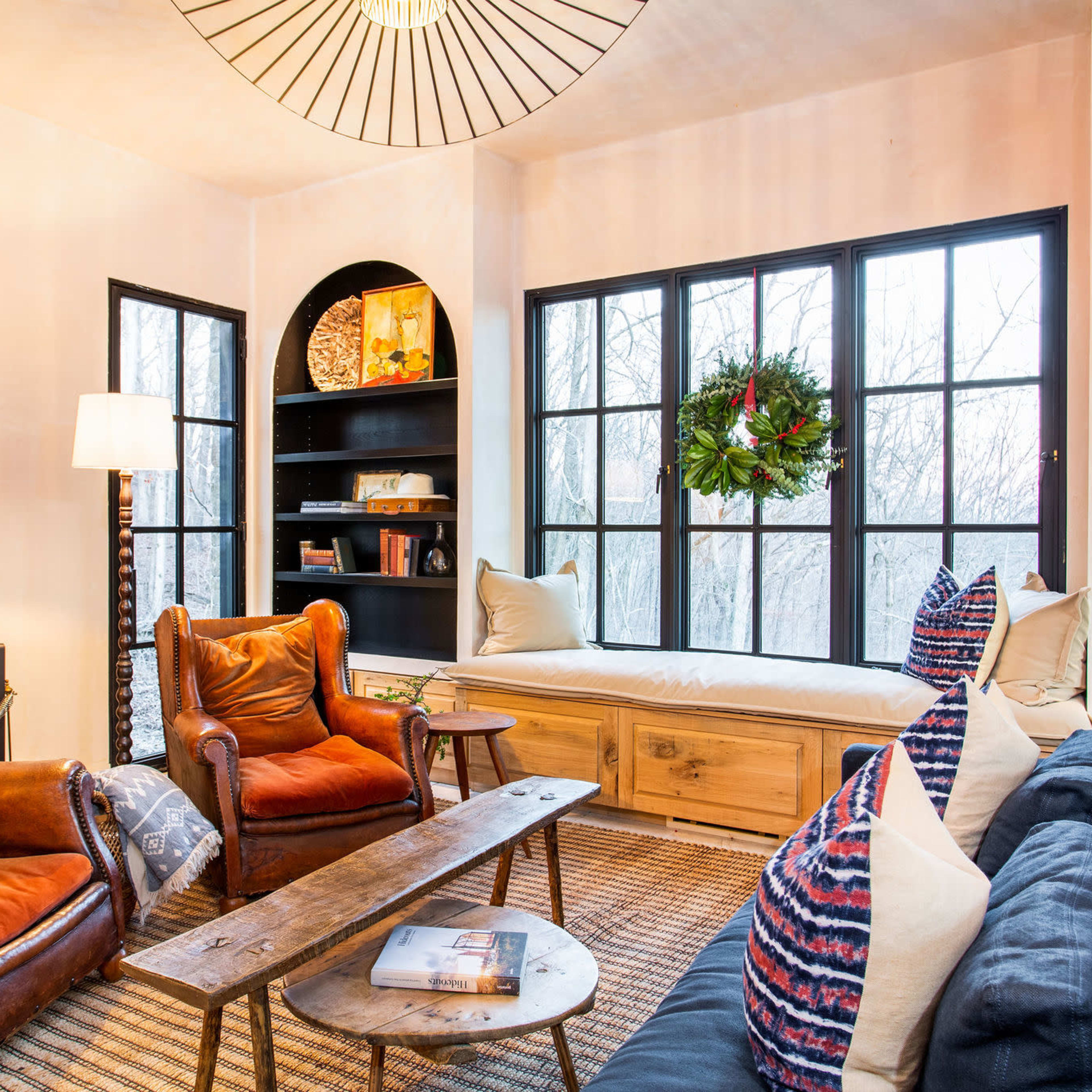 A cozy living room with two brown leather armchairs, a wooden coffee table, and a built-in bench under large windows, decorated with a wreath.
