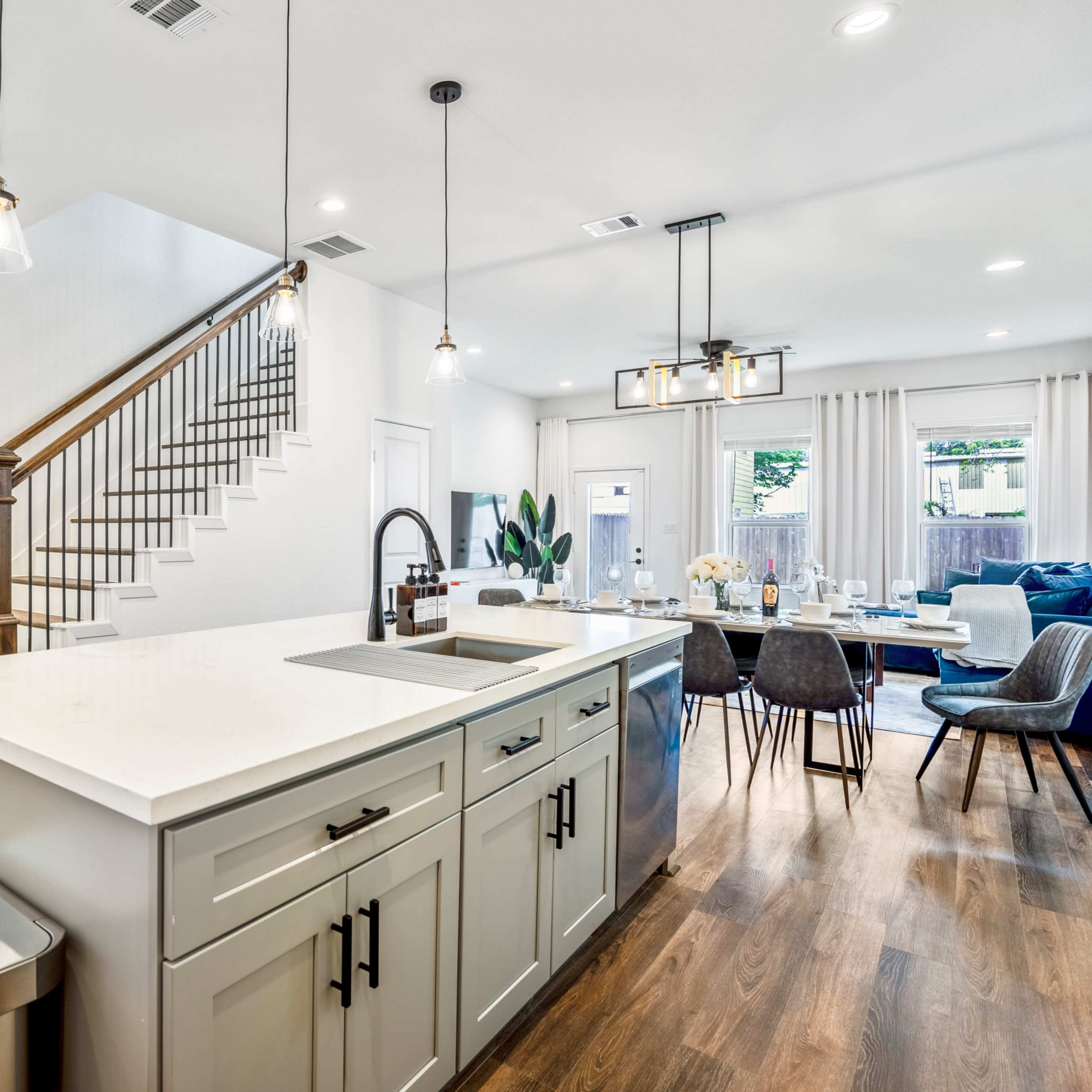 A modern kitchen features an island with a sink, surrounded by a dining area and a staircase leading to an upper floor.