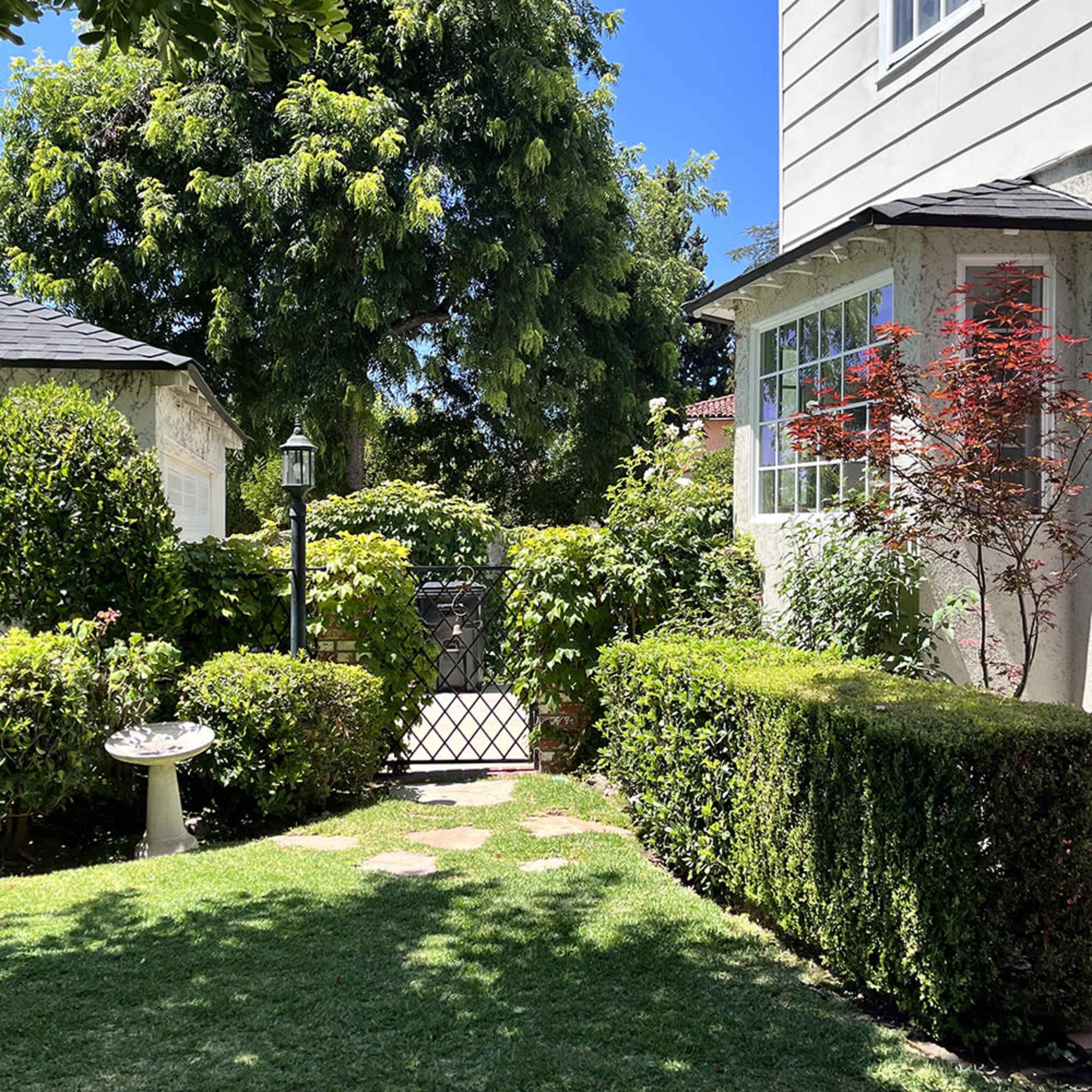 A garden pathway leads to a wrought-iron gate surrounded by lush greenery and neatly trimmed hedges.