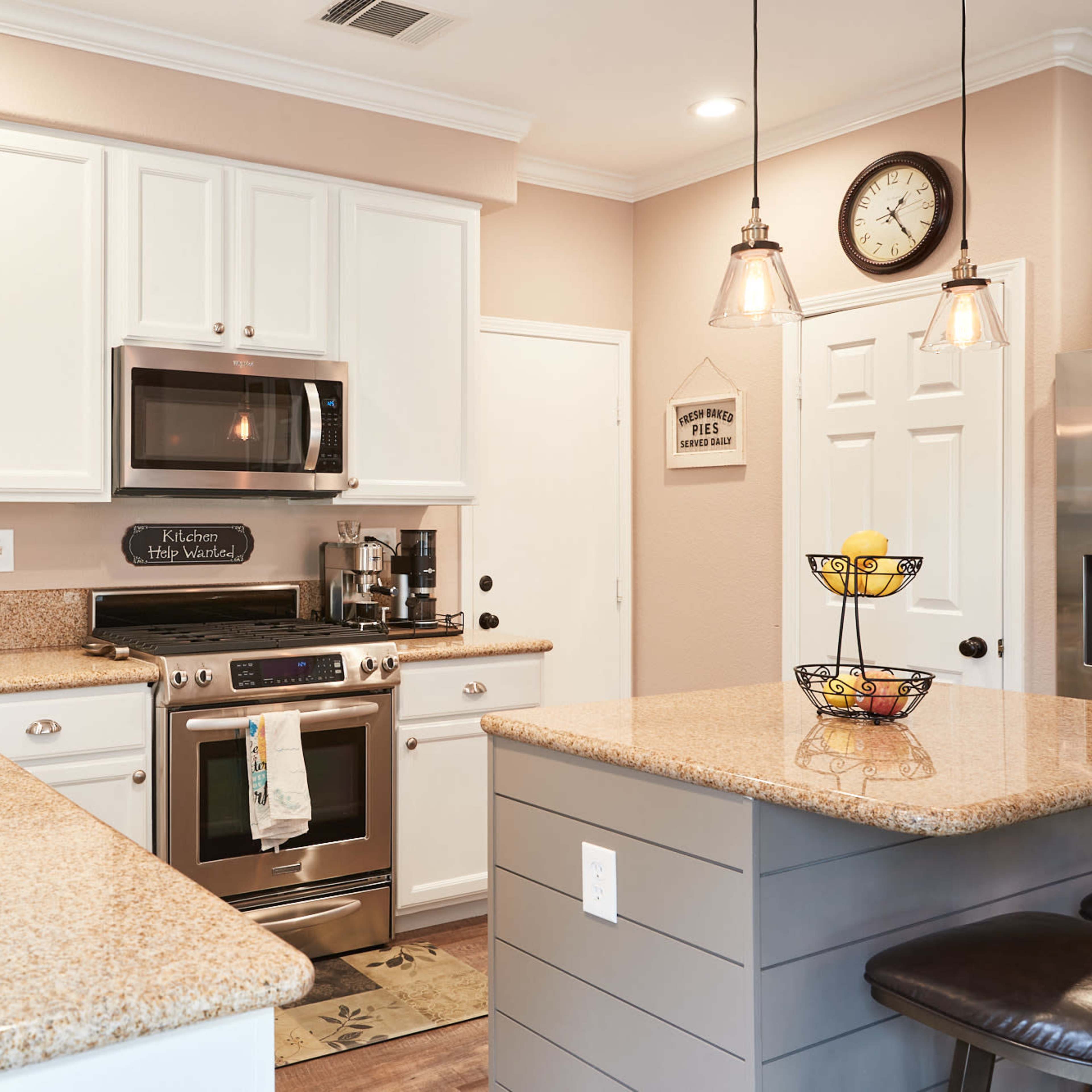 A modern kitchen with white cabinetry, stainless steel appliances, and a granite countertop island.