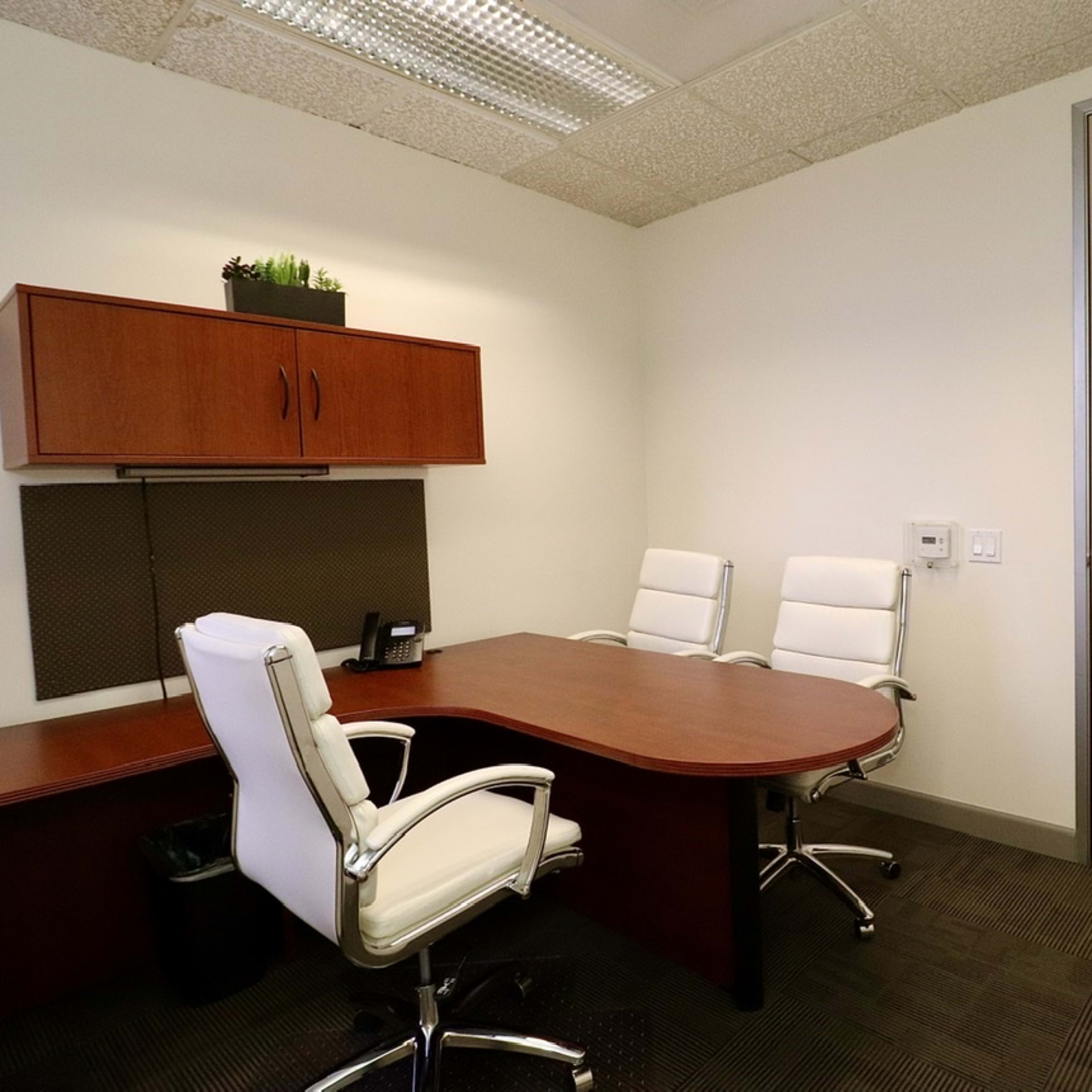 A small office with a wooden desk, two white chairs, and a door leading outside.