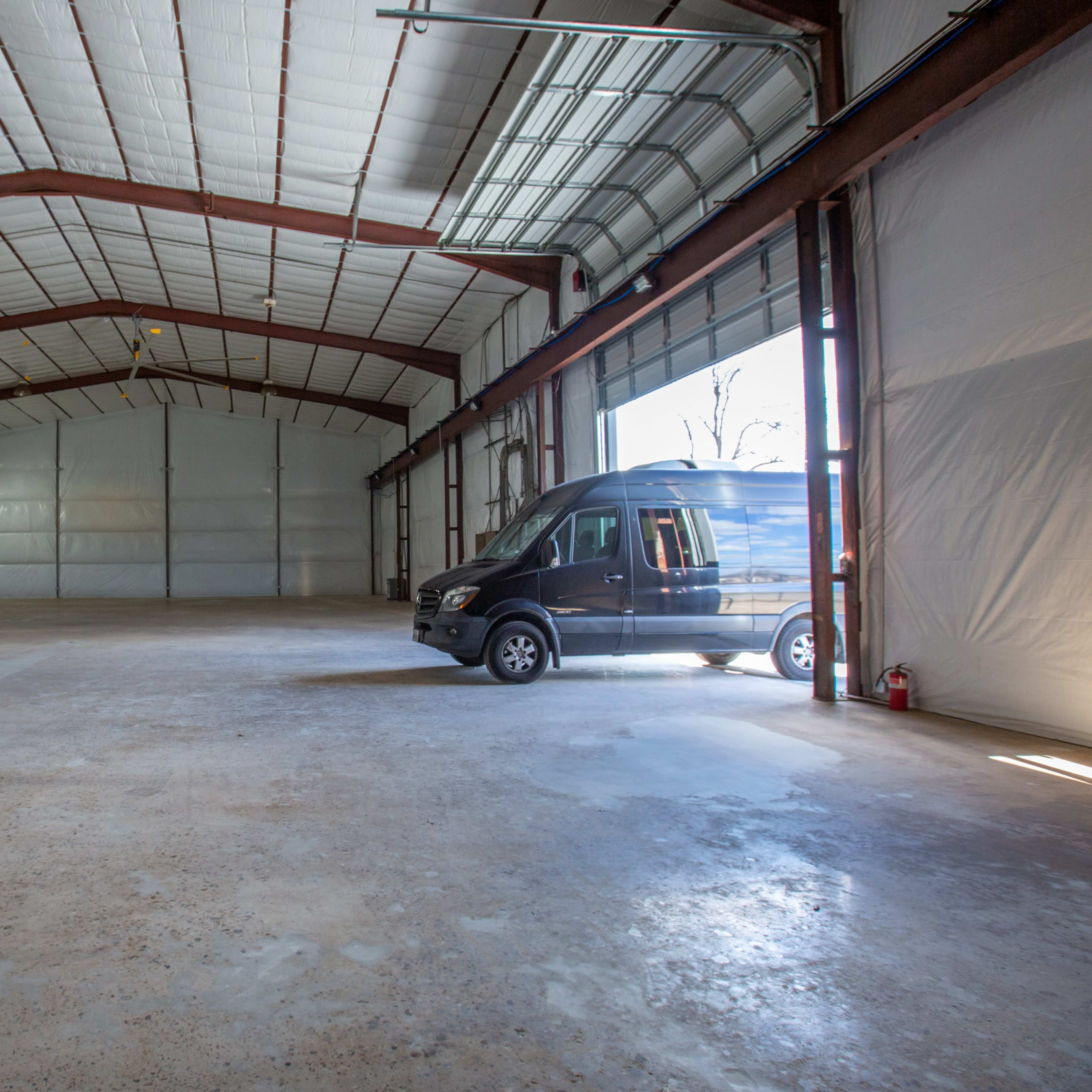 A large, empty warehouse with a high ceiling and a van parked near the entrance.