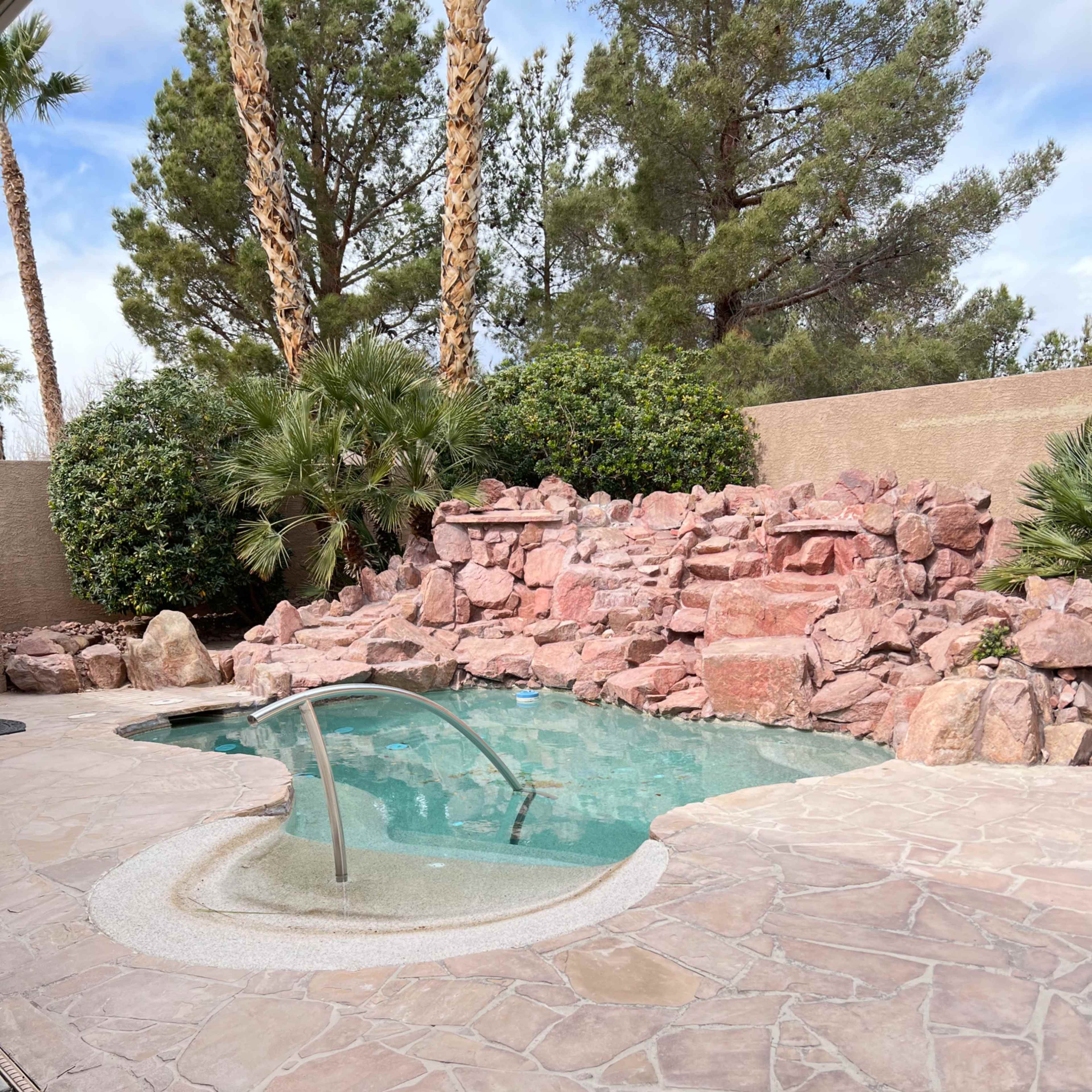 A small swimming pool surrounded by stone and rock landscaping, with palm trees in the background.