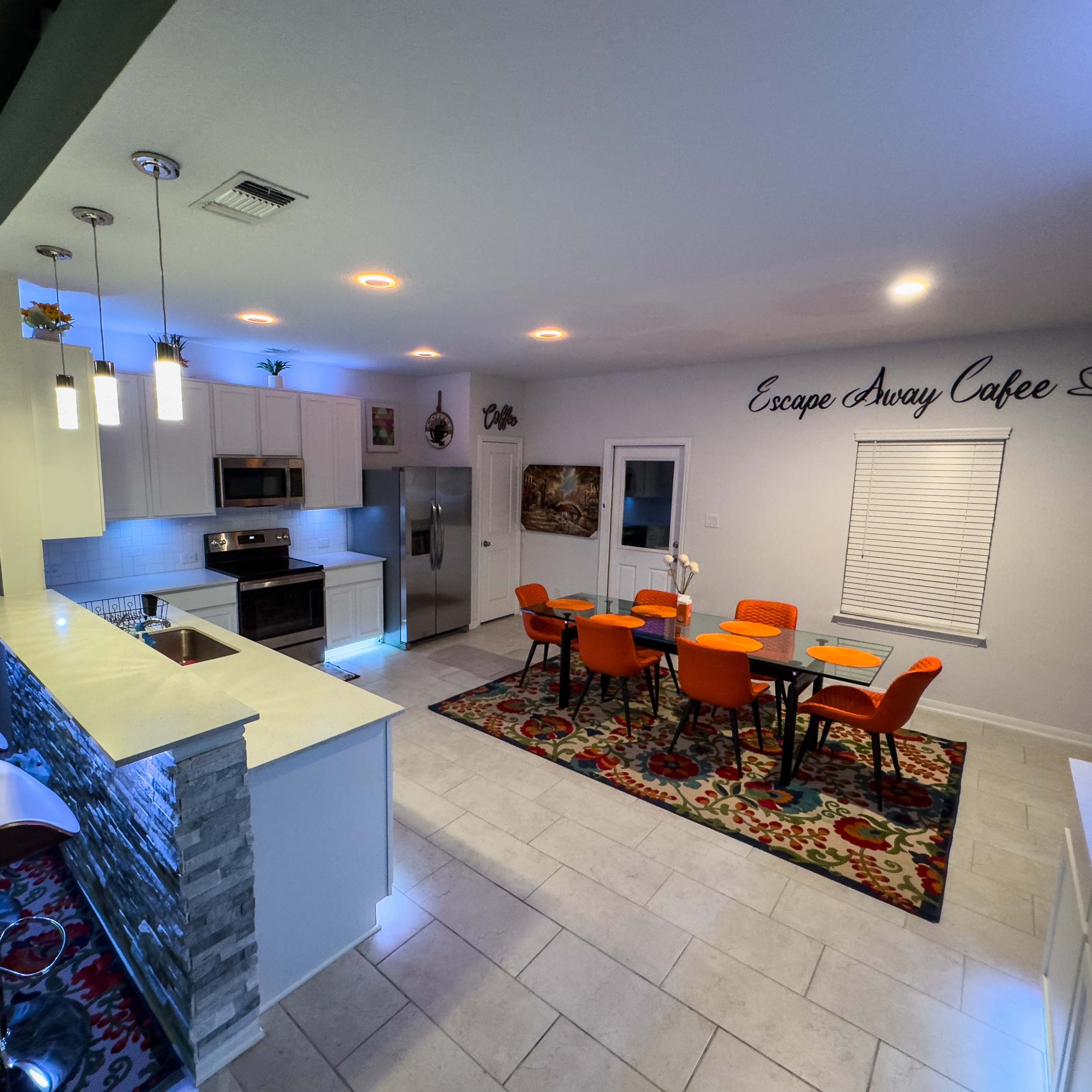 A modern kitchen and dining area features sleek counter seating, an island, and a round dining table surrounded by orange chairs.